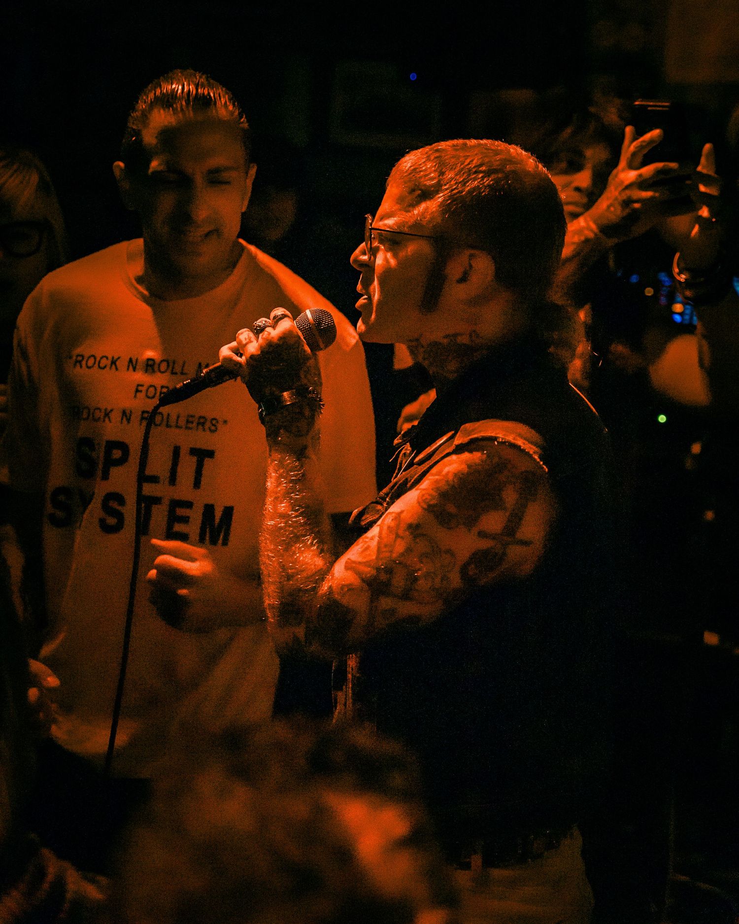 Dimly lit concert crowd with orange lighting and band merchandise visible.