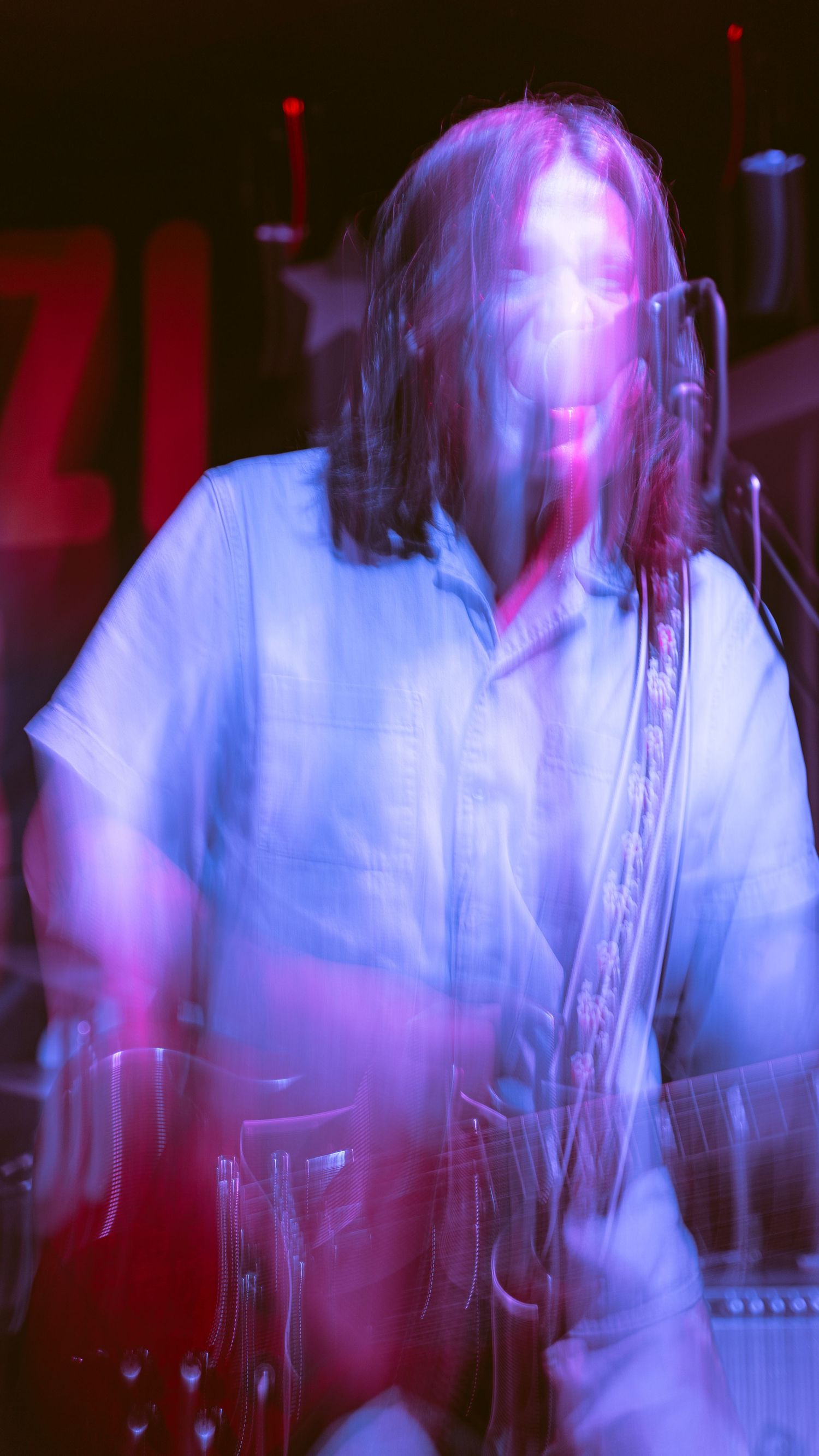Musician performing with guitar under blue and purple stage lighting creating a motion blur effect.