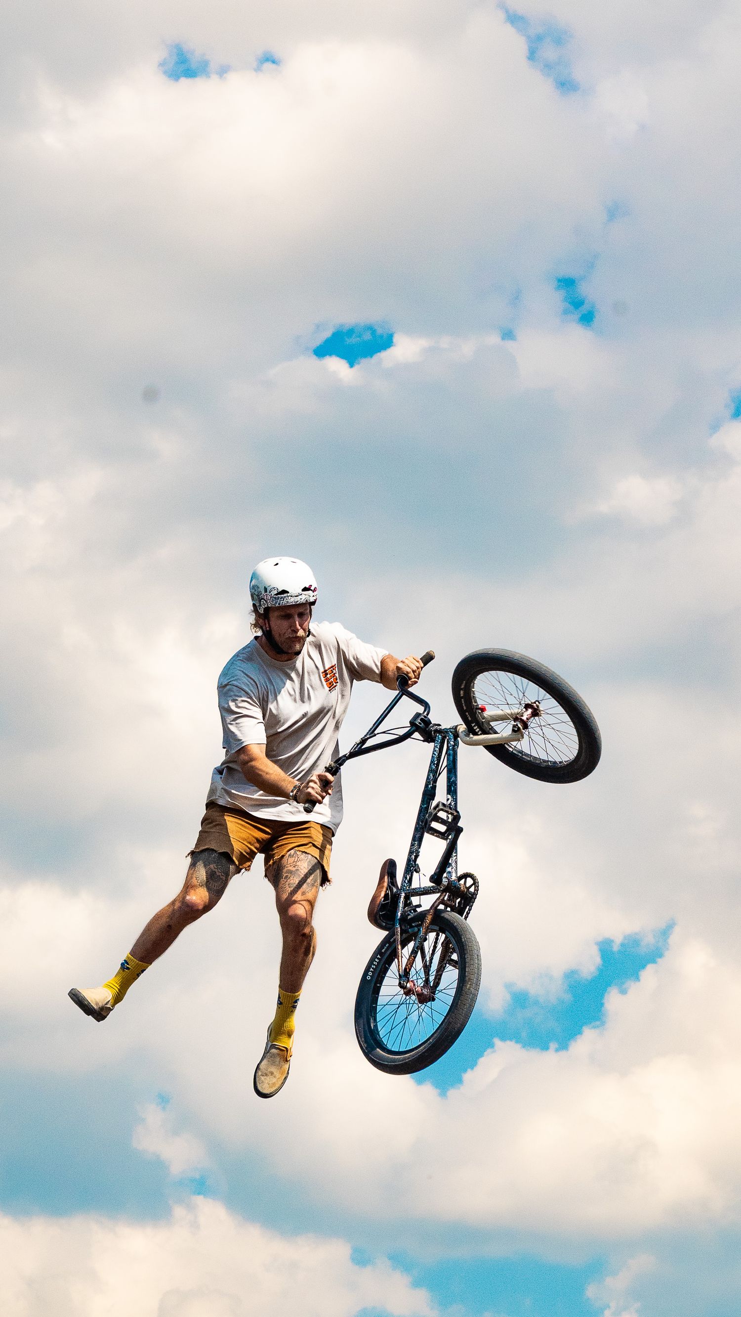 BMX rider separates from bike during aerial stunt with cloudy sky backdrop.