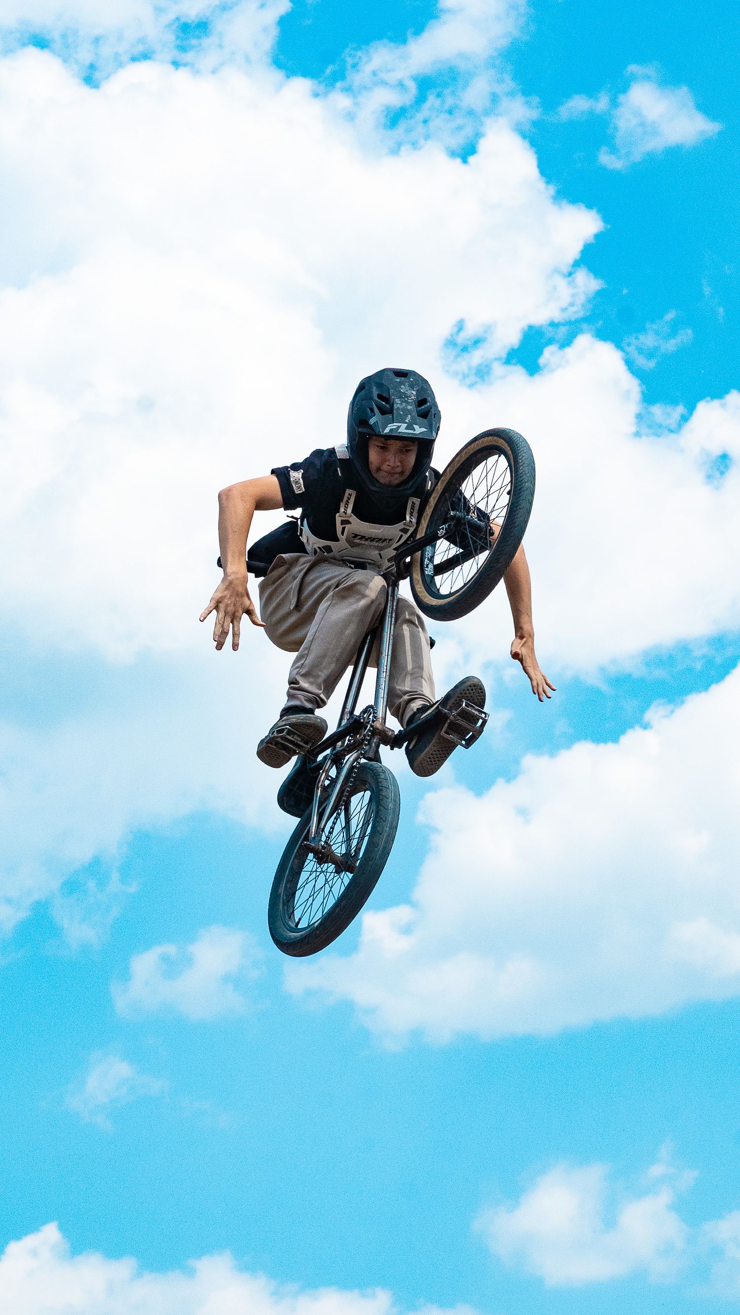 Skilled BMX rider executes mid-air rotation against cloudy blue sky.