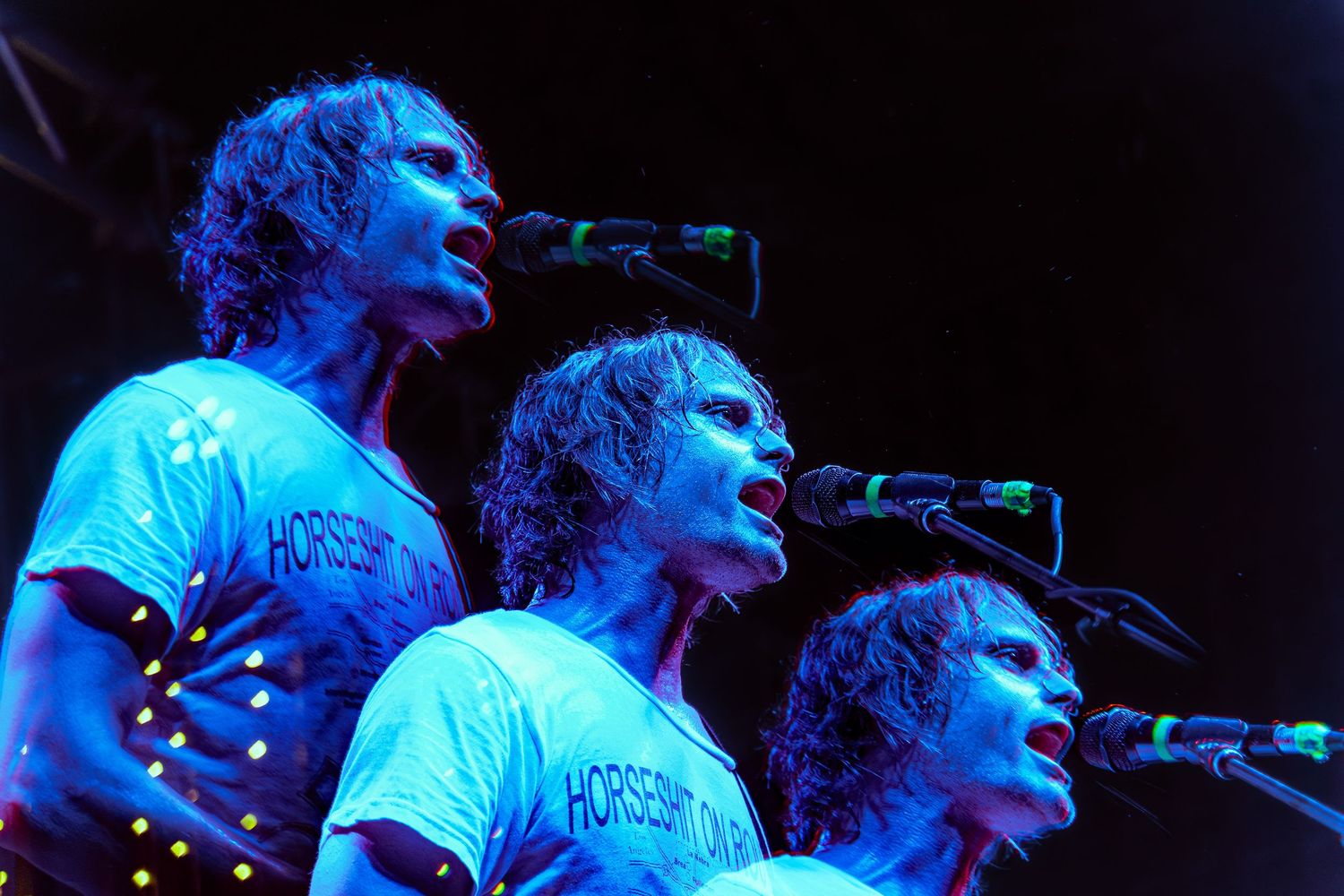 A performer singing and playing guitar on stage under blue lighting at a concert performance.