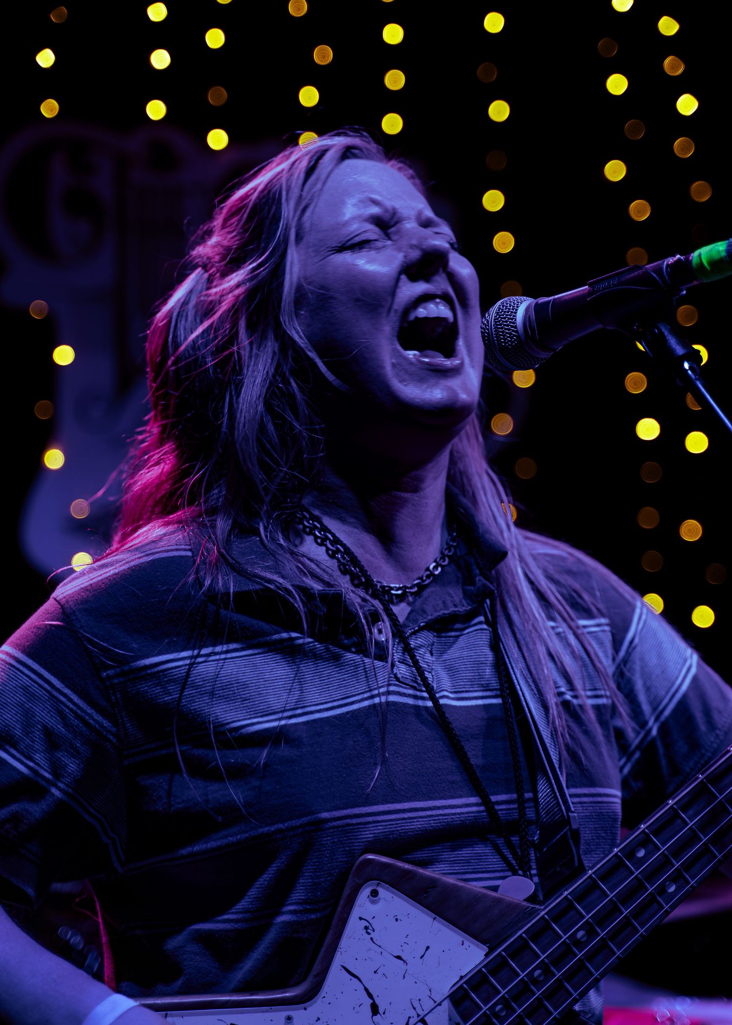 Electric guitarist performing on stage with colored lighting and bokeh effects in the background.