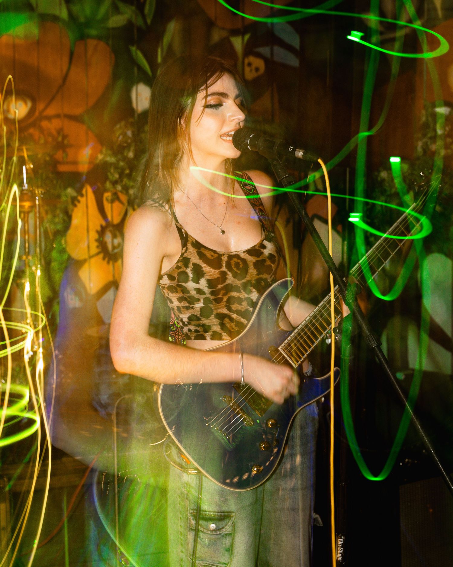 Guitar performance on stage with green and orange lighting effects creating dreamy atmosphere.