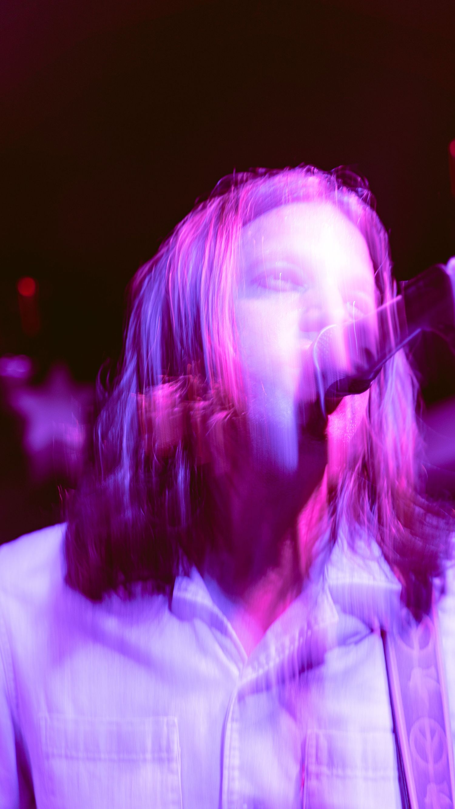Concert performer bathed in vibrant purple stage lighting with motion blur creating an ethereal effect.