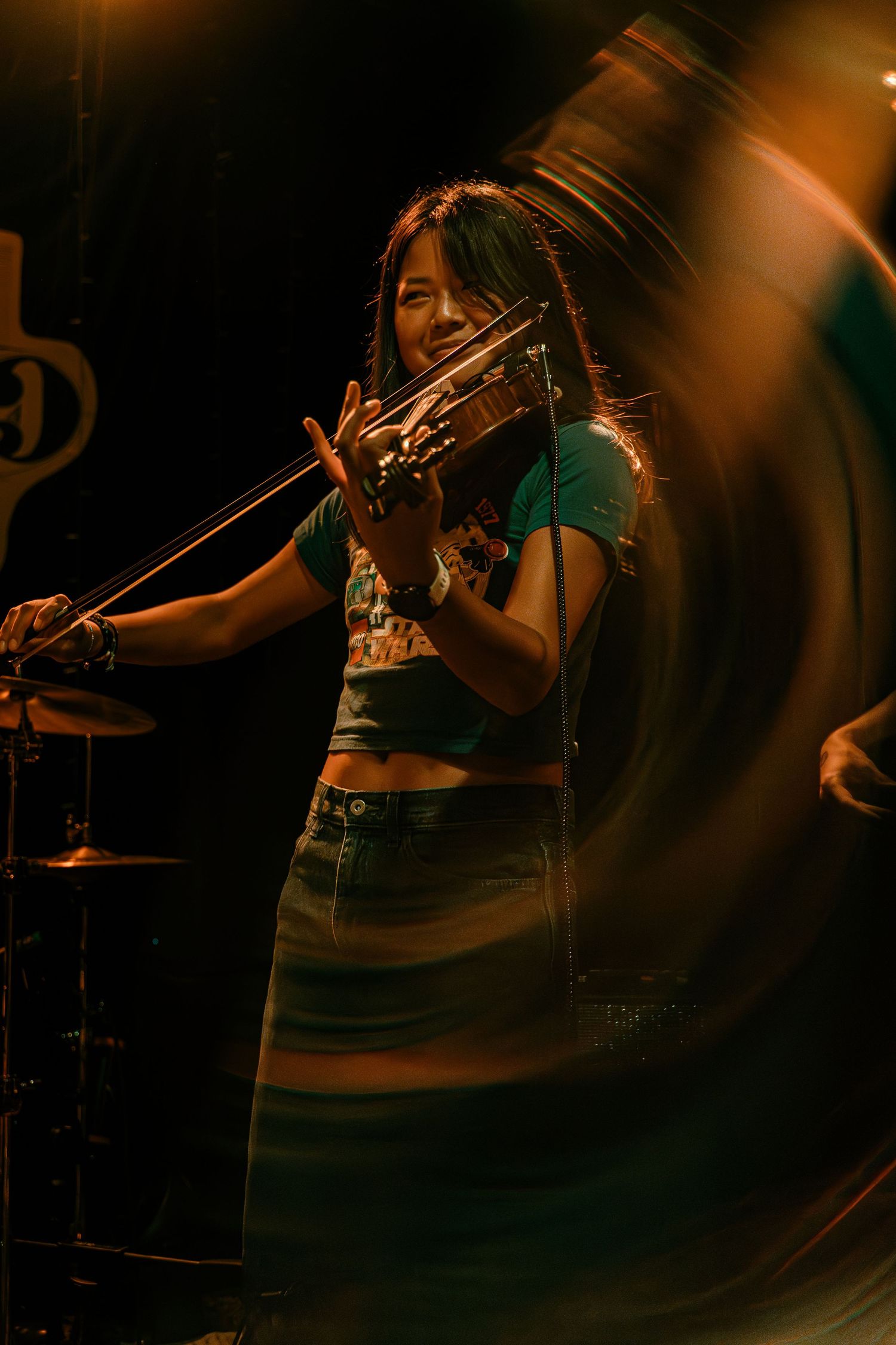 A musician plays violin on stage with dramatic lighting creating an atmospheric performance scene.