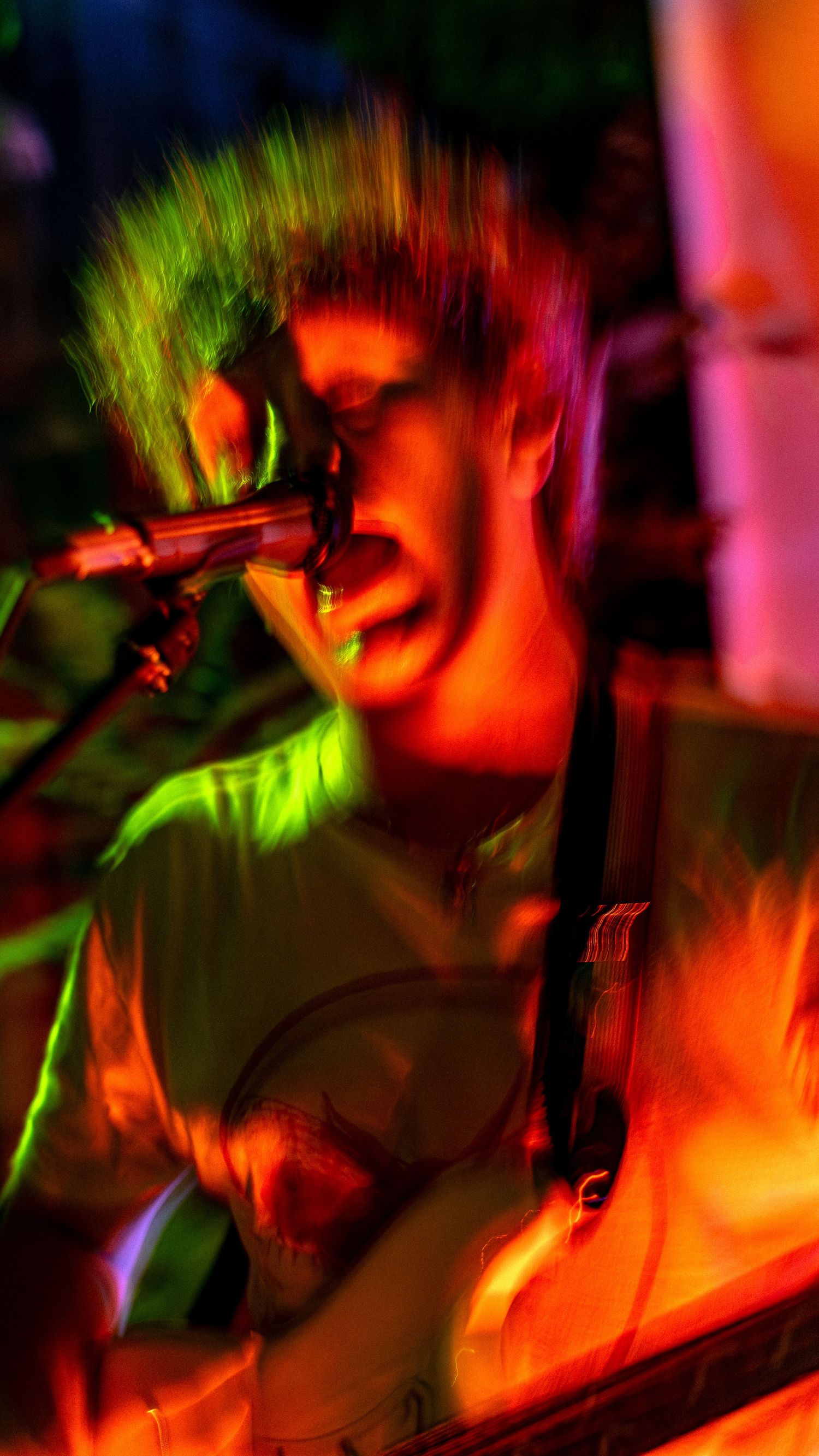 Concert performer singing into microphone under dramatic neon green and red stage lighting.