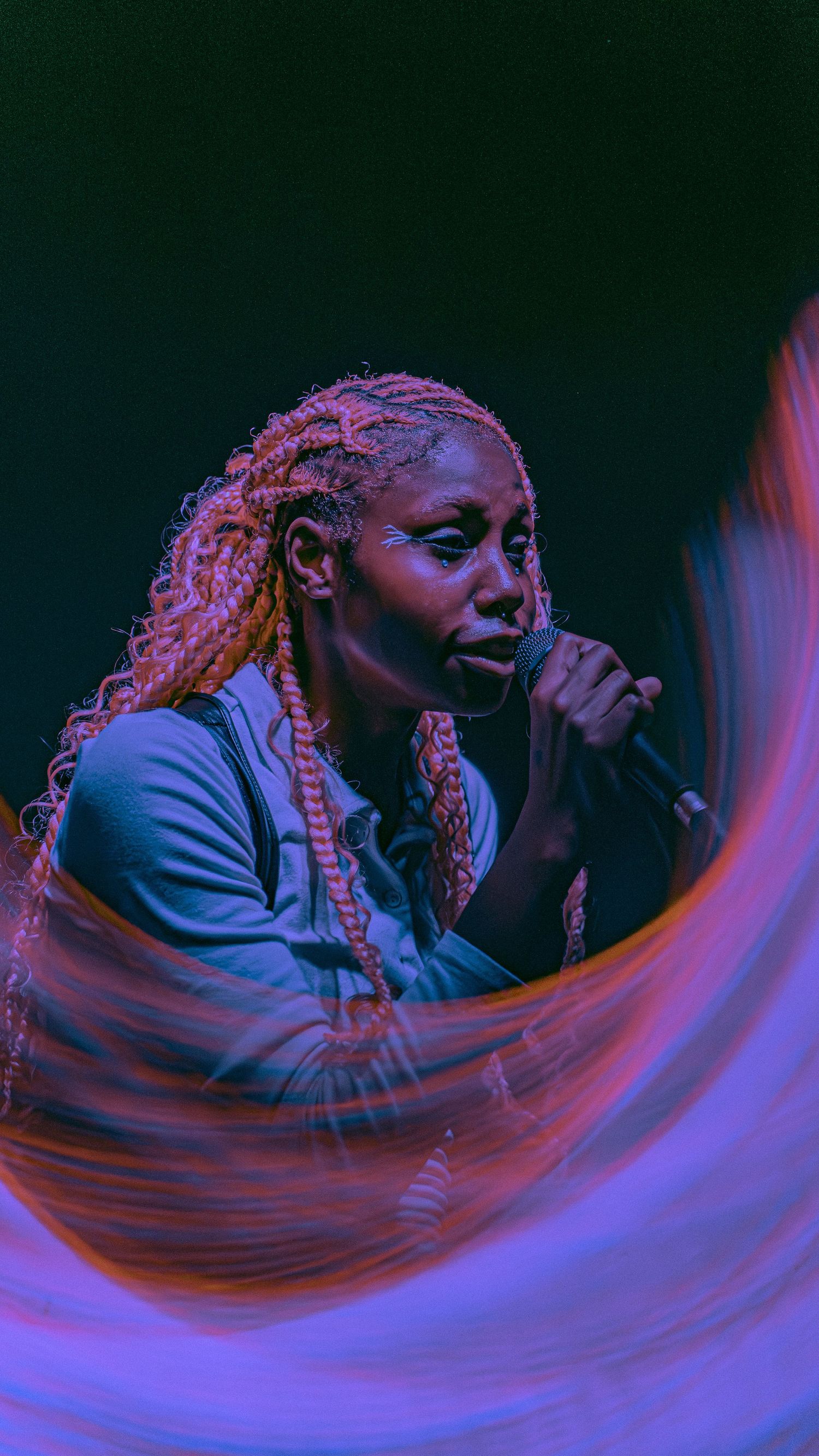 Artist performs on stage with dramatic lighting effects in blue and orange while singing into microphone.