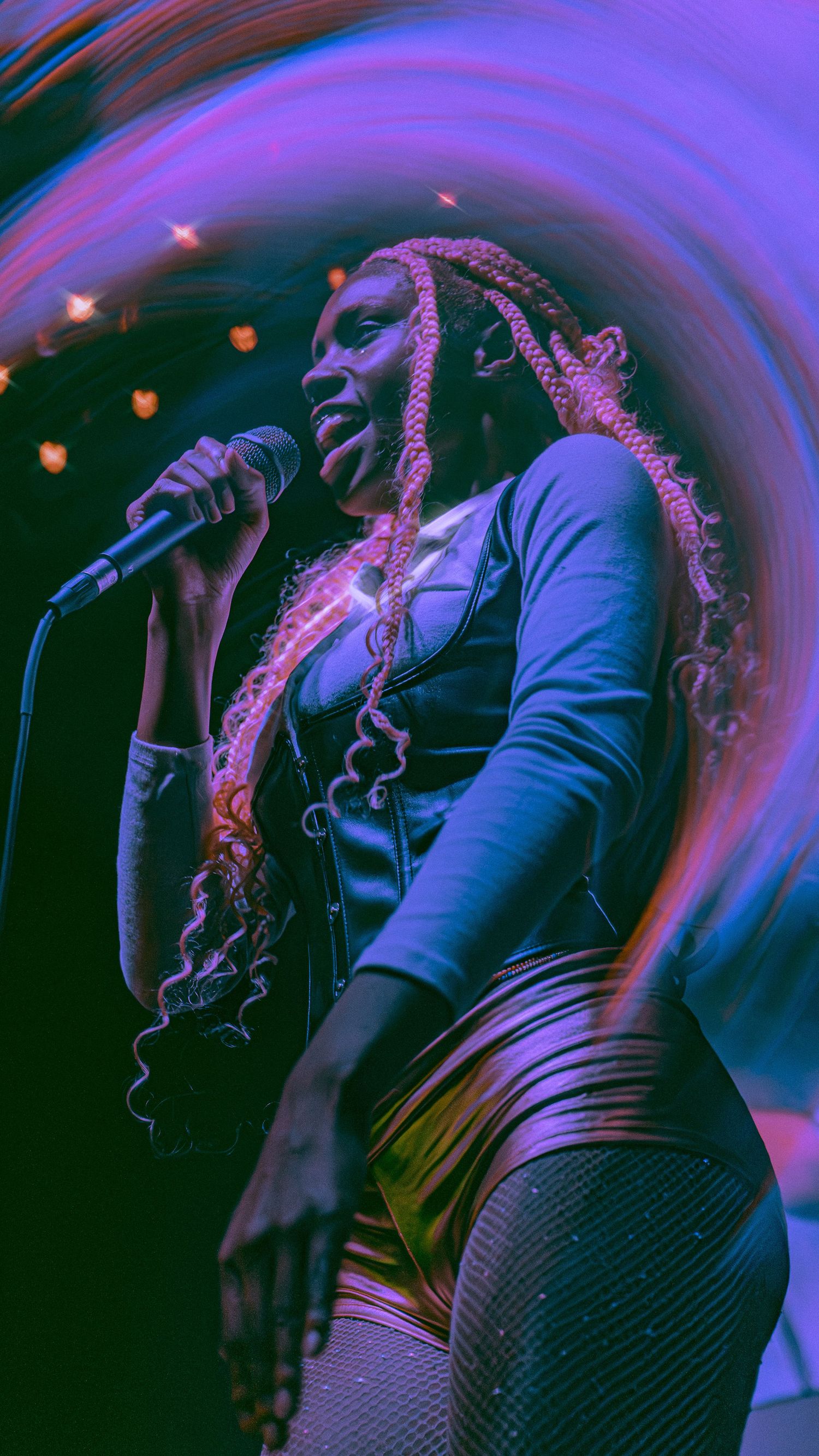 Performance photo showing a microphone silhouetted against vibrant purple and blue lighting effects during a live show.