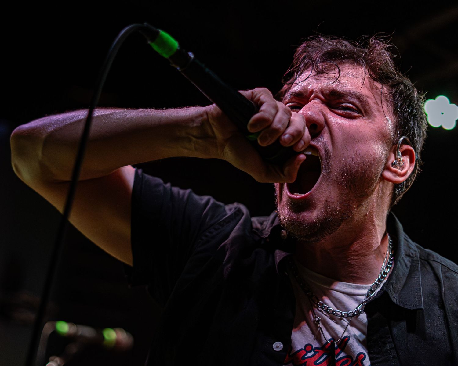 A performer with a microphone sings passionately on stage against a dark background in an emotional musical performance.
