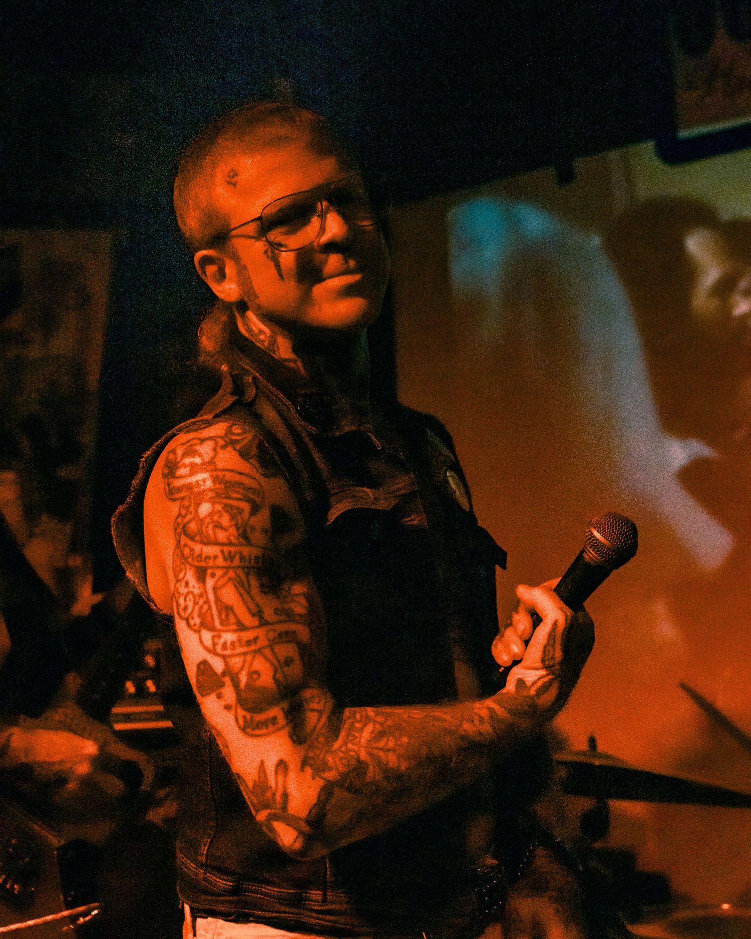 Tattooed performer on stage illuminated by warm orange lighting.