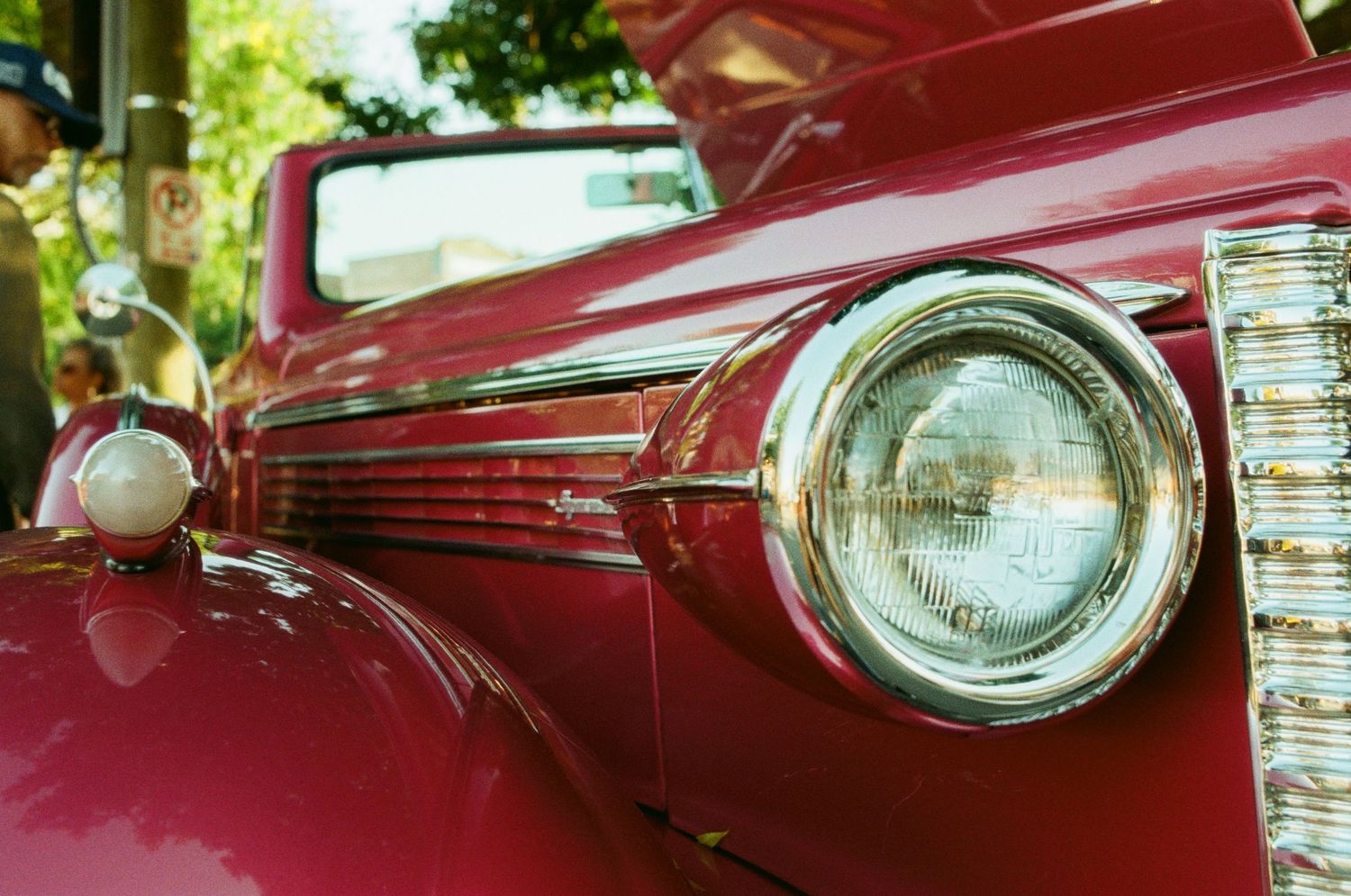 Close-up view of a vintage red car's chrome headlight and front fender details showing classic automotive styling.