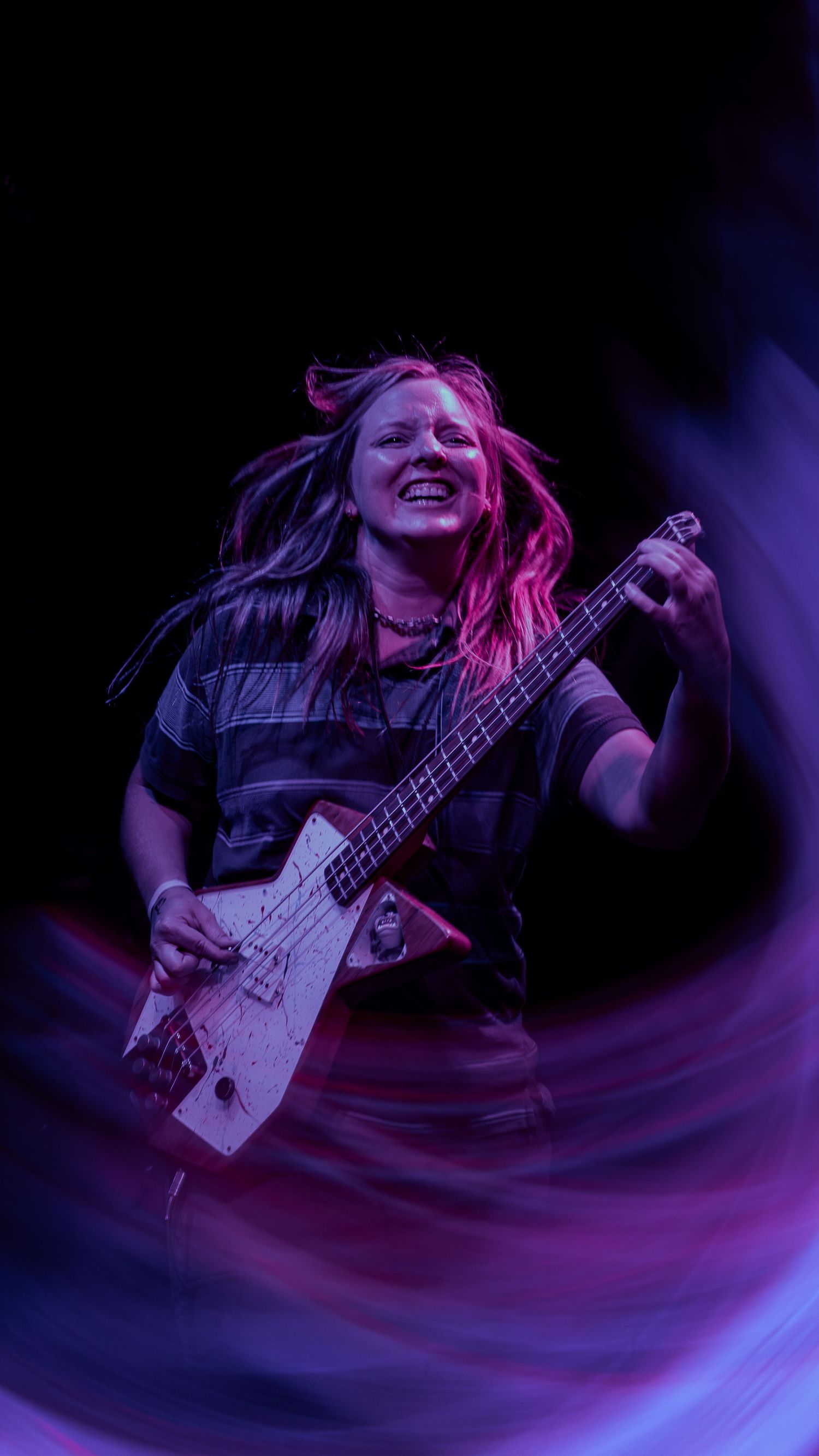 Musician plays bass guitar on stage with dramatic purple lighting and motion blur effects in performance action shot.