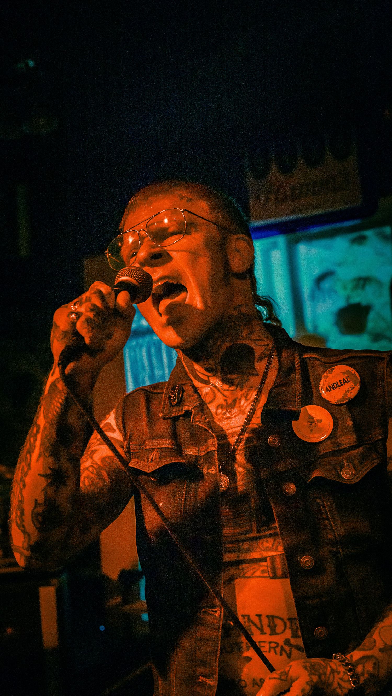 Concert performer silhouetted in dramatic orange stage lighting while singing into a microphone.