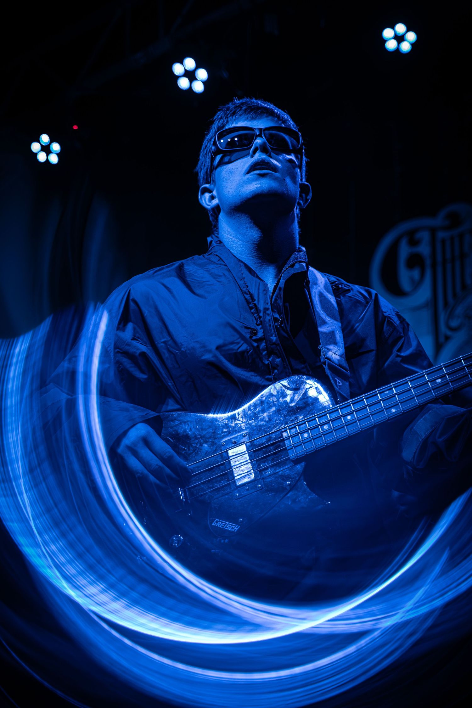 Long exposure shot shows blue light trails behind bassist playing instrument in dark concert venue.