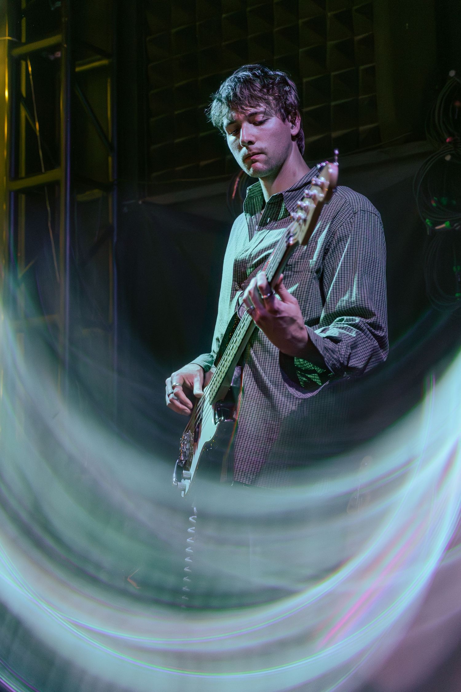 Multiple exposure shot of guitarist playing on stage with ethereal swirling light effects.
