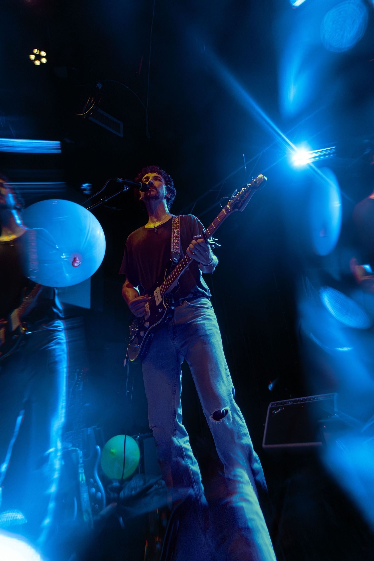 Musician performs with electric guitar silhouetted against dramatic blue stage lighting during live concert performance.