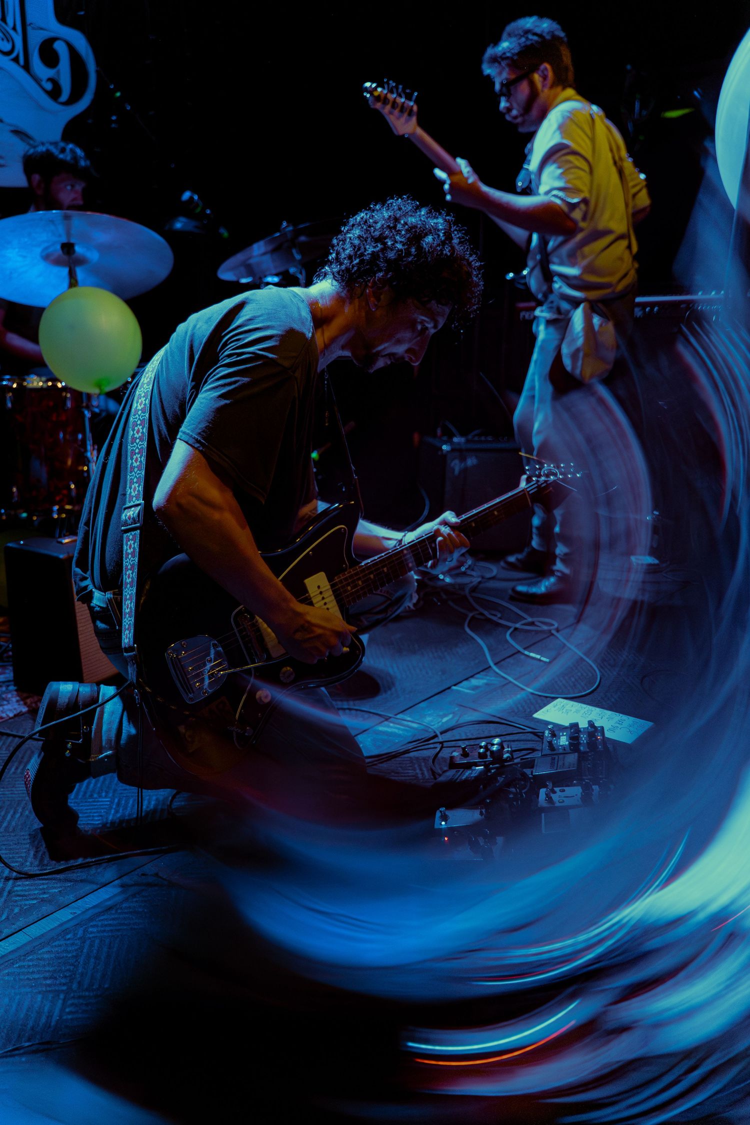 Musicians perform on stage under dramatic blue lighting with instruments and equipment visible in sequence.