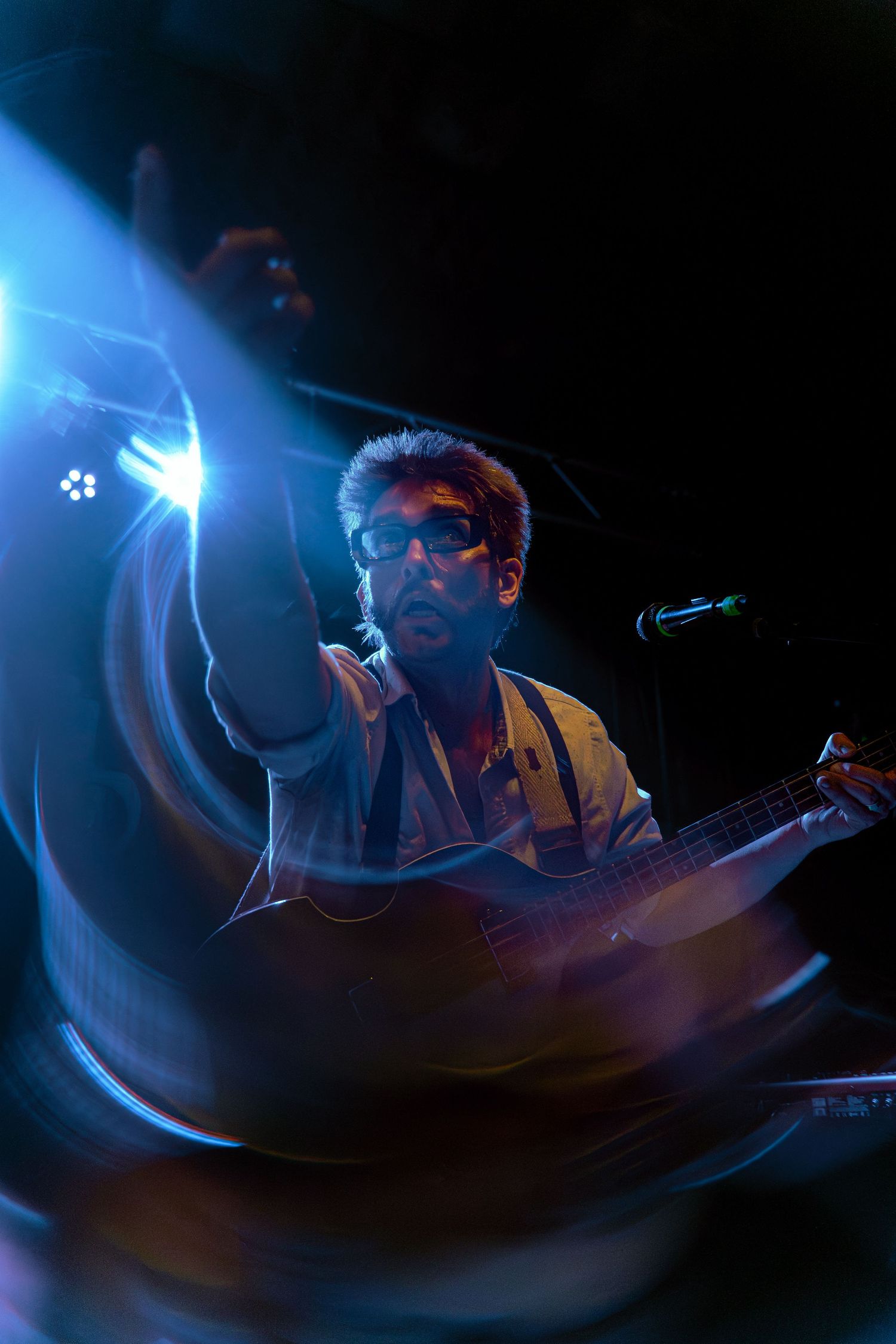 Musician performs in dark lighting with dramatic blue spotlights creating an atmospheric concert ambiance.