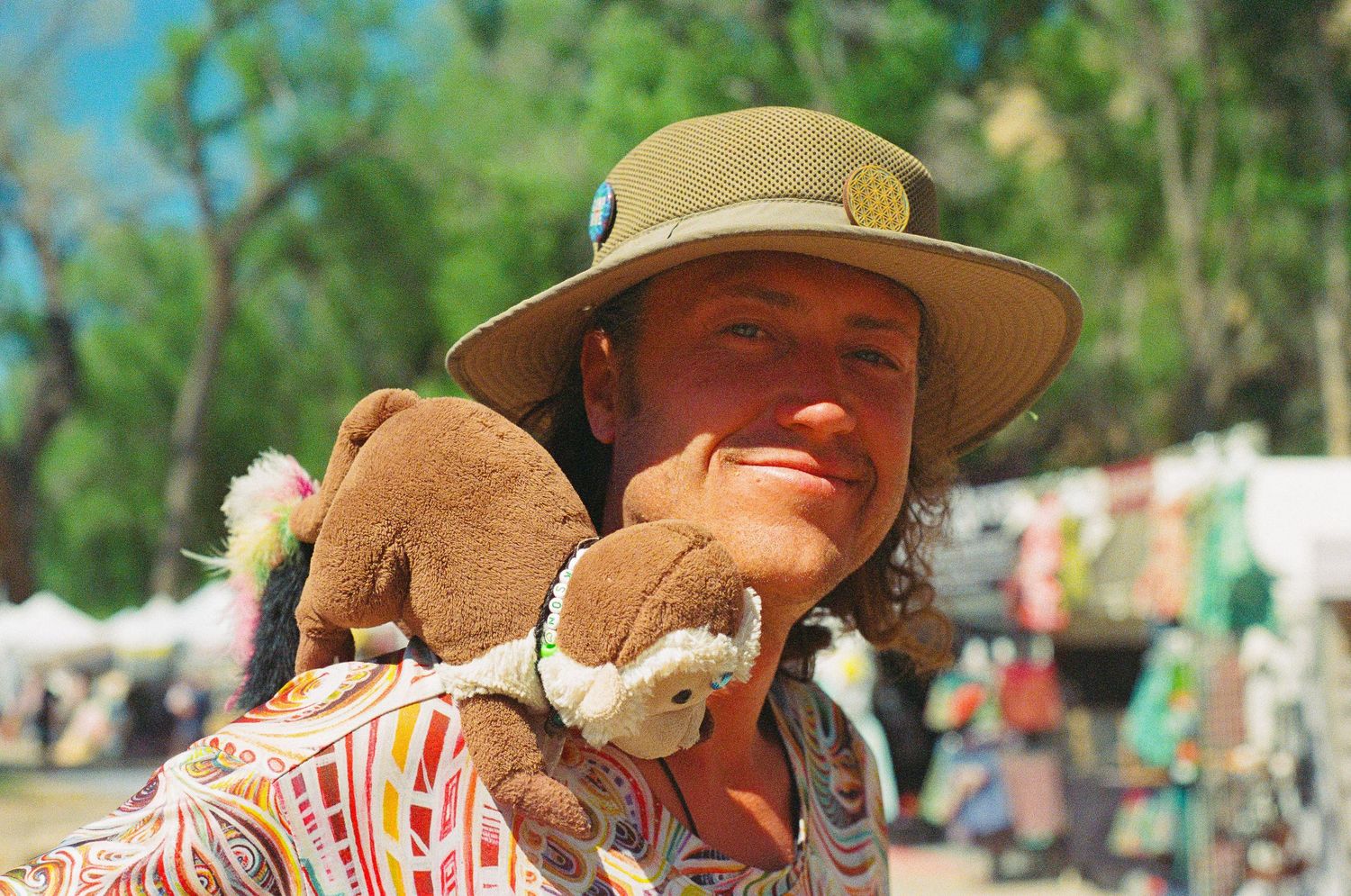 Person in a wide-brimmed hat holding stuffed animals at an outdoor festival.