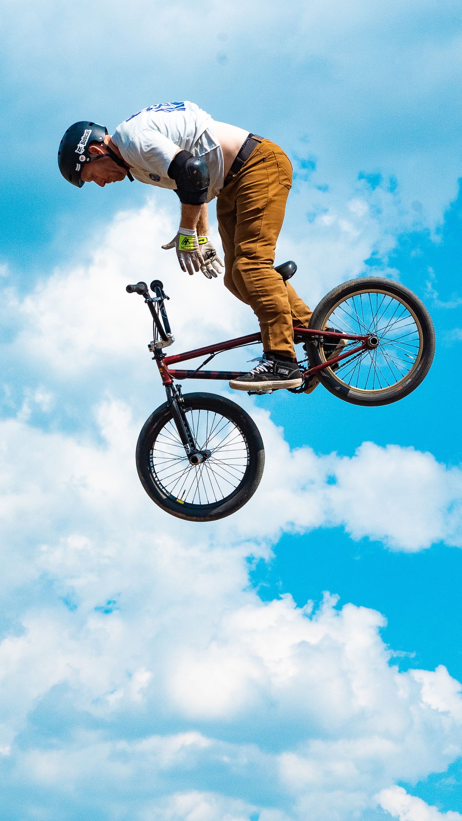 Skilled BMX rider performs horizontal aerial trick against bright cloudy sky.