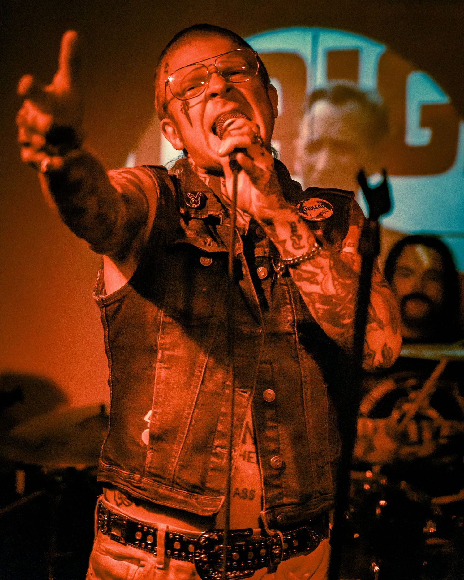 Performer in denim jacket passionately singing on stage with dramatic orange lighting and raised hand gesture.