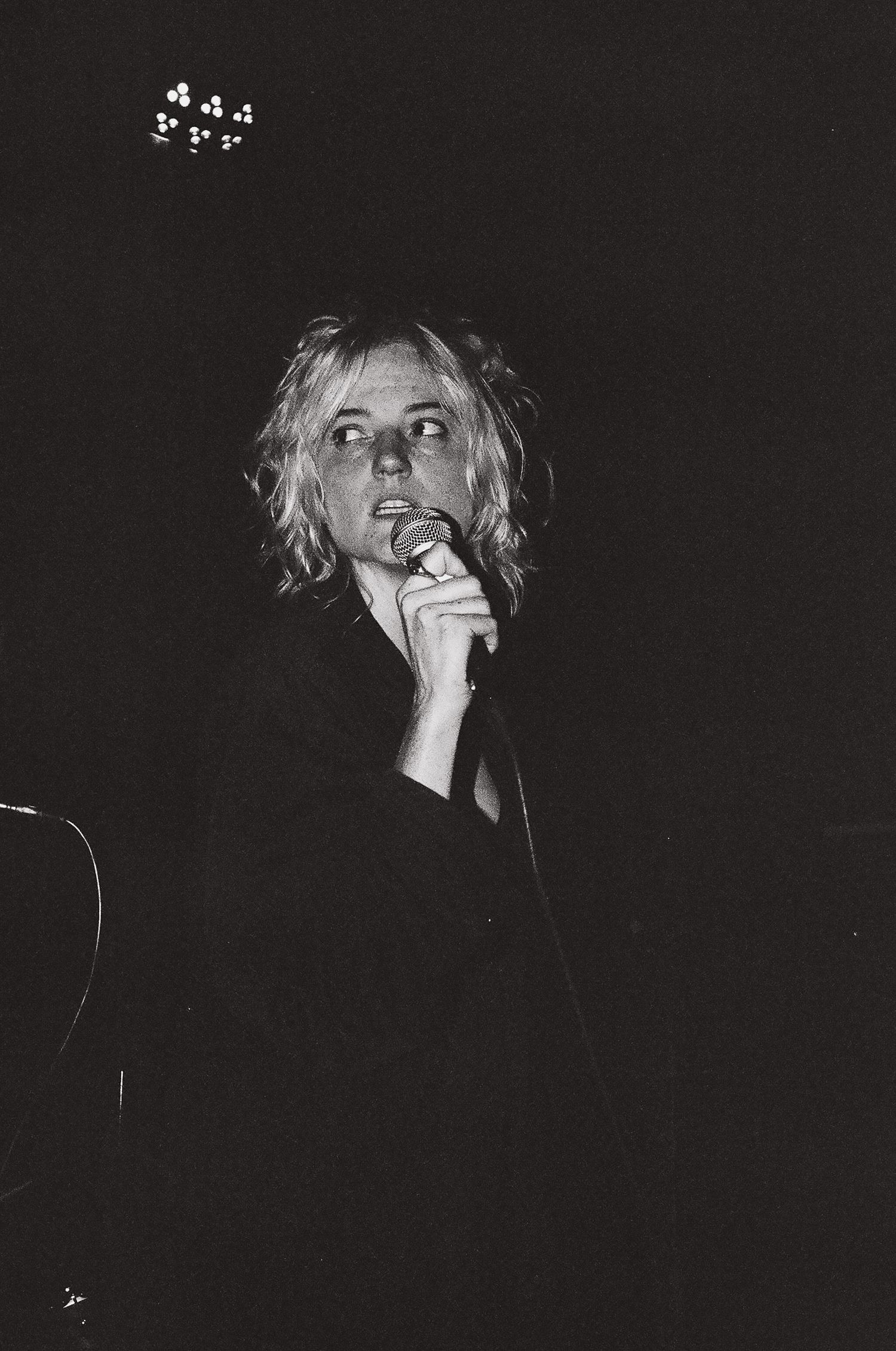 Black and white concert photo capturing performer singing into microphone under stage lights.
