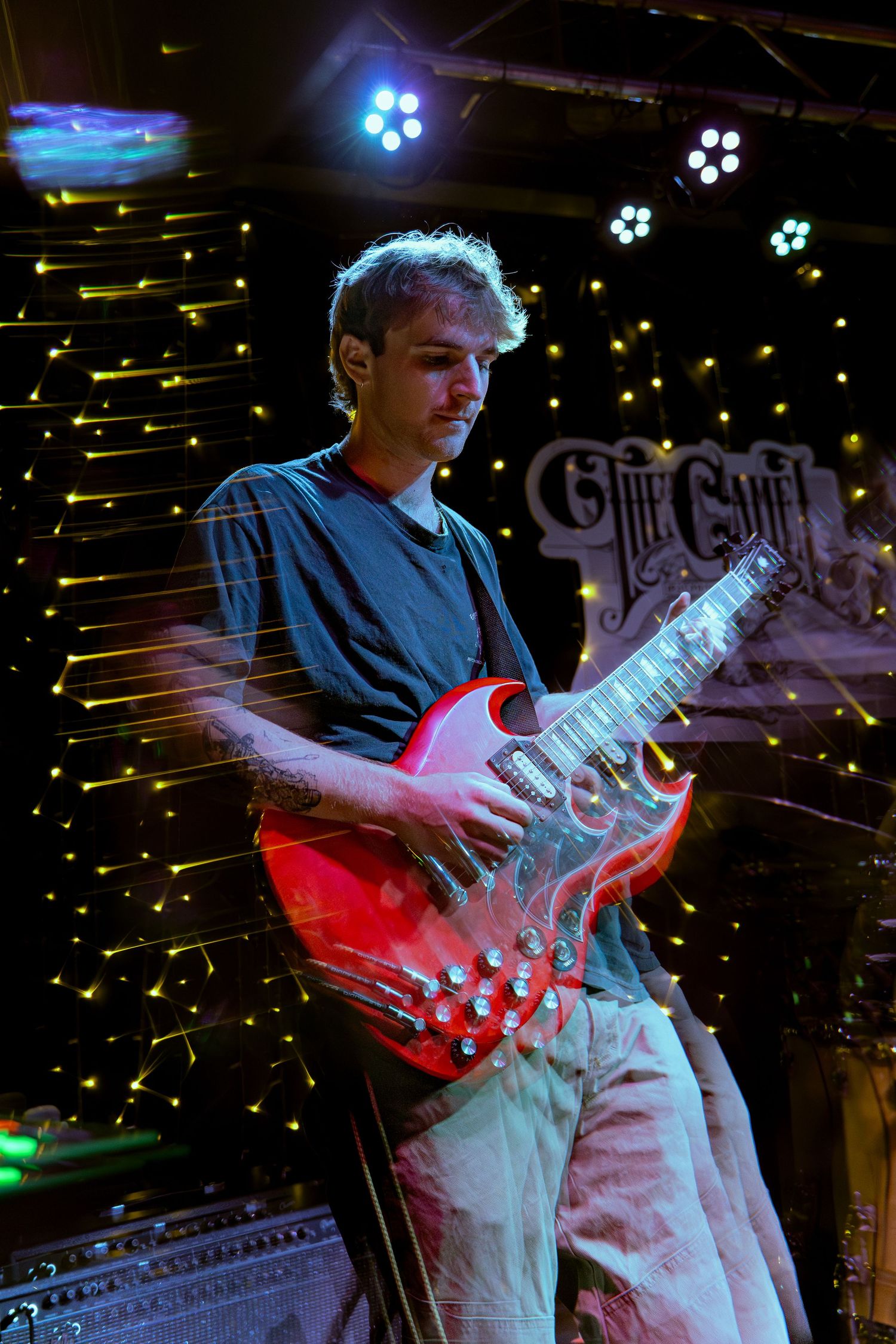 Guitarist performing on stage with red lighting and illuminated string lights creating a dramatic concert atmosphere.