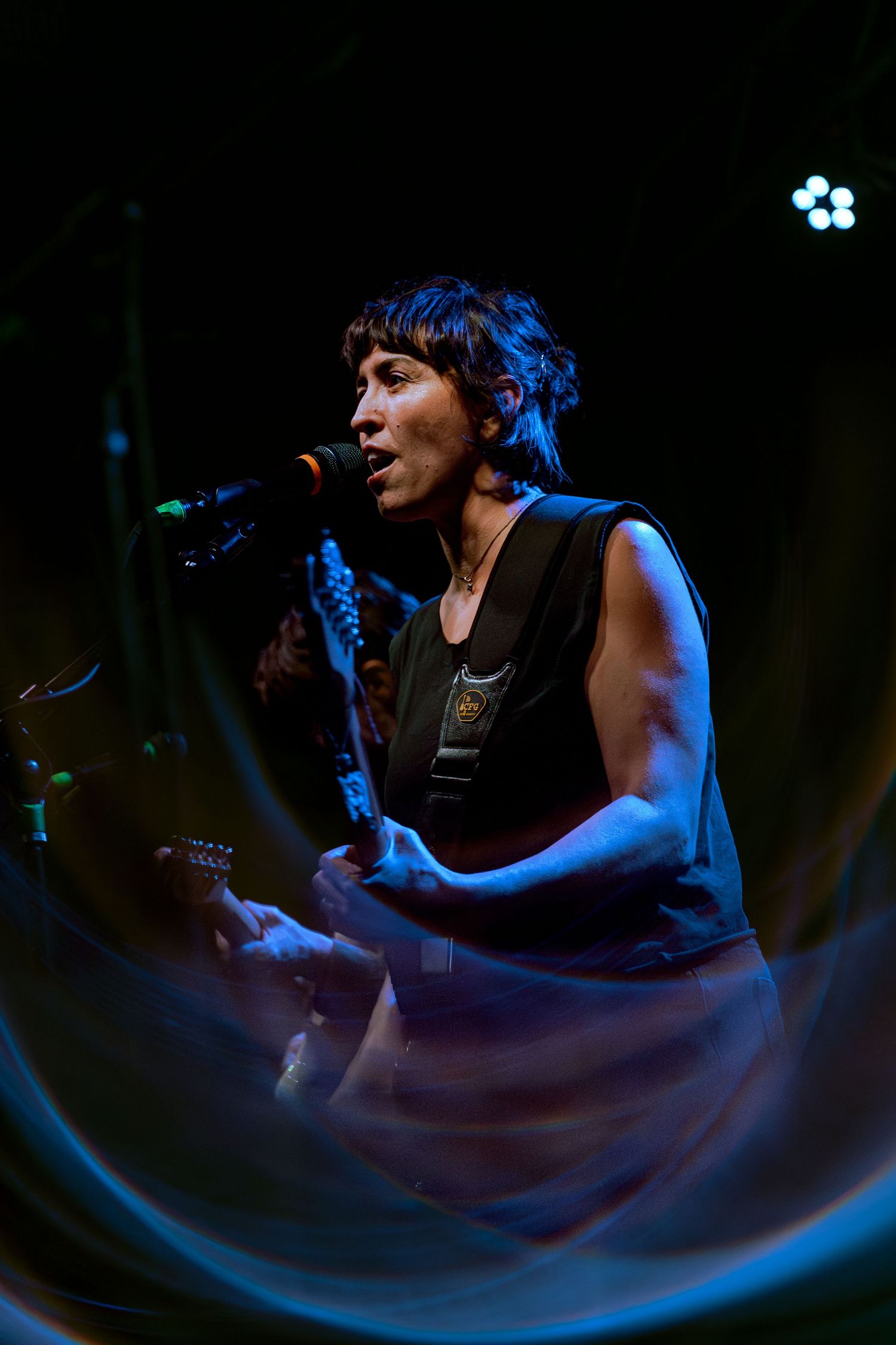 Performer singing and playing guitar on dark stage illuminated by blue lighting during intimate concert performance.