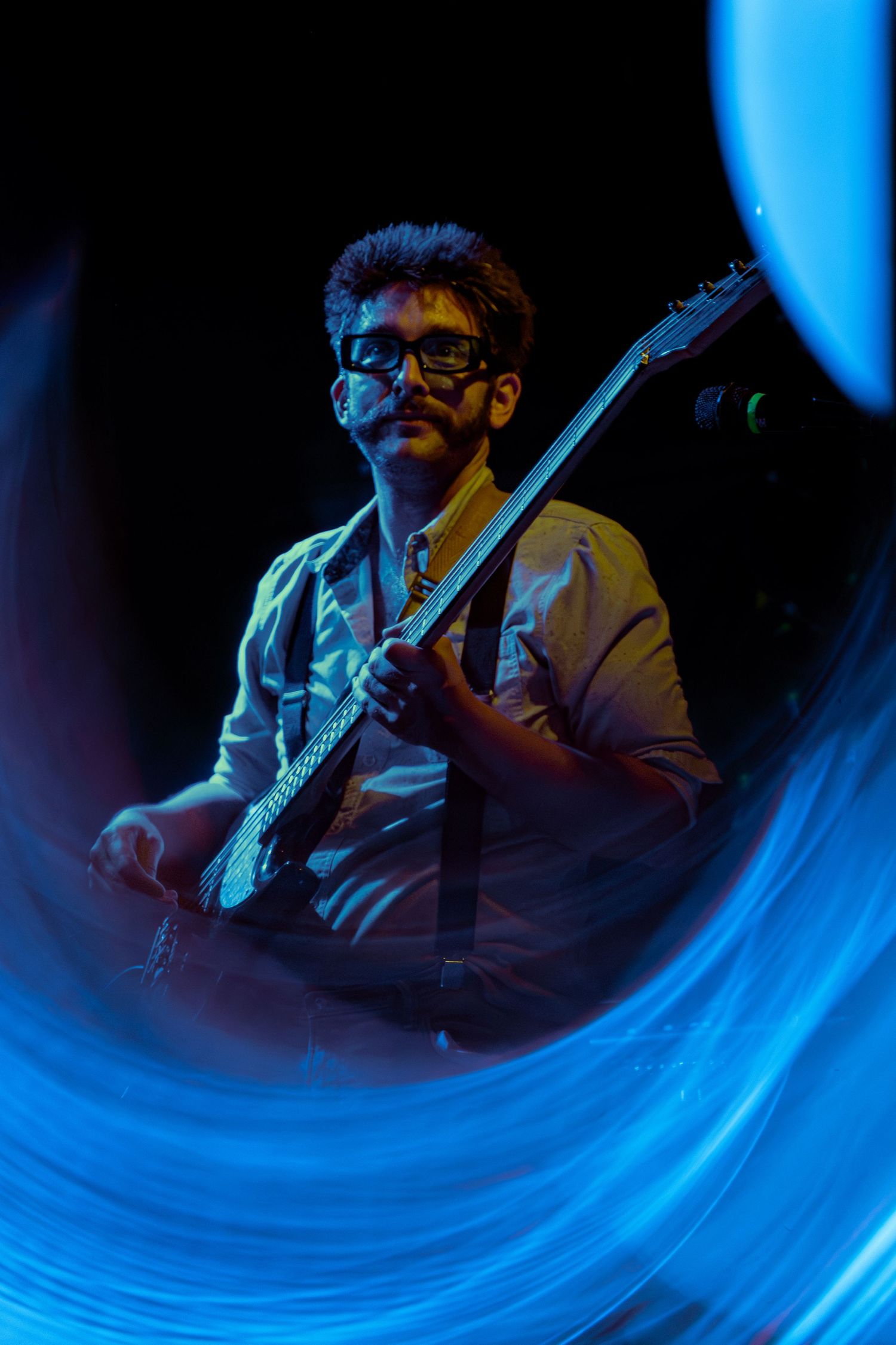 Guitarist performs on stage with dramatic blue lighting and motion blur effect creating a dynamic swirling pattern.