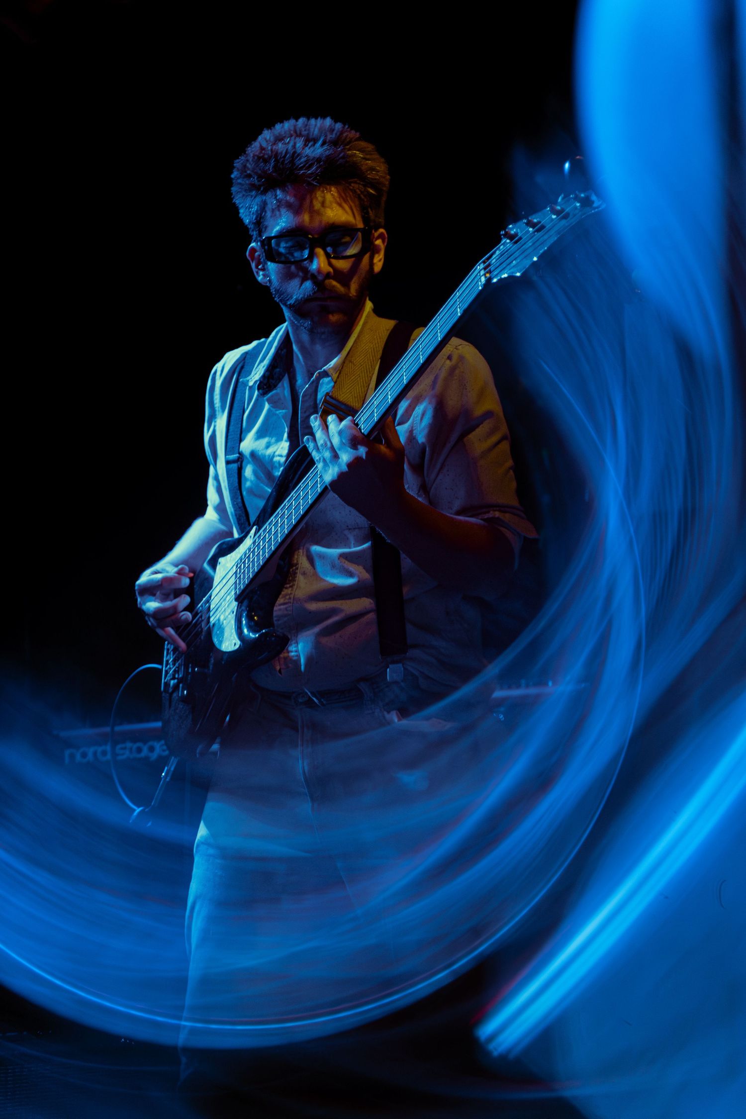 Motion blur captures a guitarist performing in dramatic blue stage lighting with multiple exposure effect.