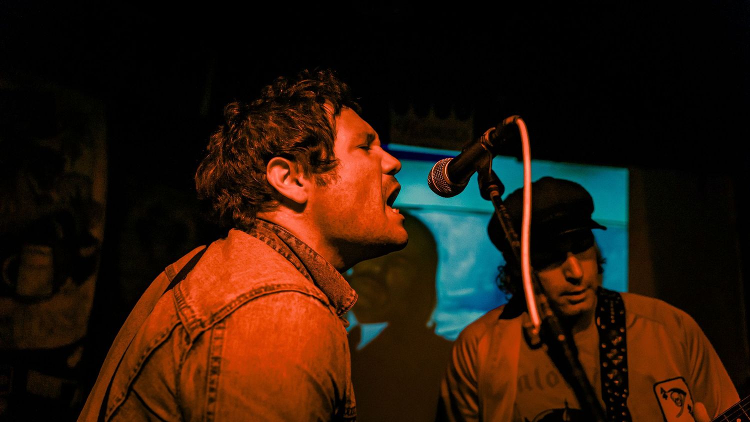 Concert venue scene bathed in orange and teal lighting creating dramatic atmosphere.