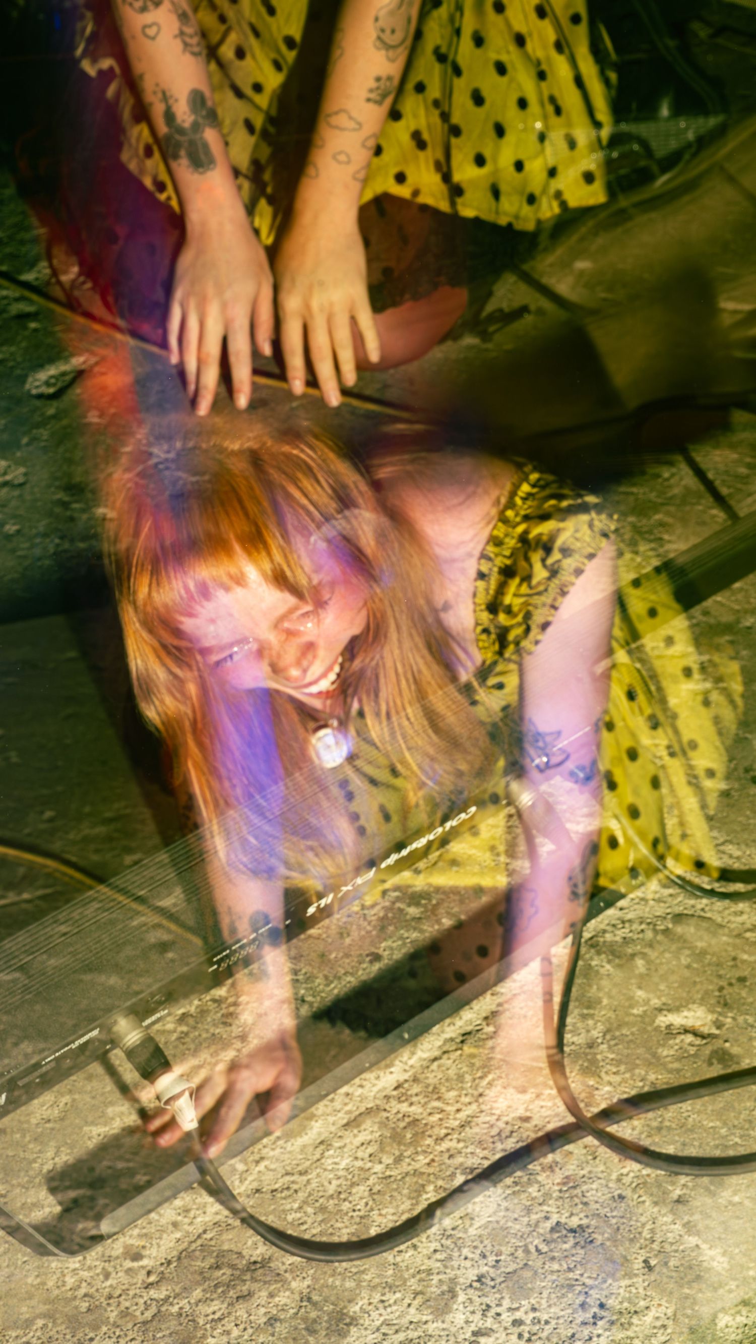 Performer in yellow polka dot dress bending down on stage with colorful lighting effects.