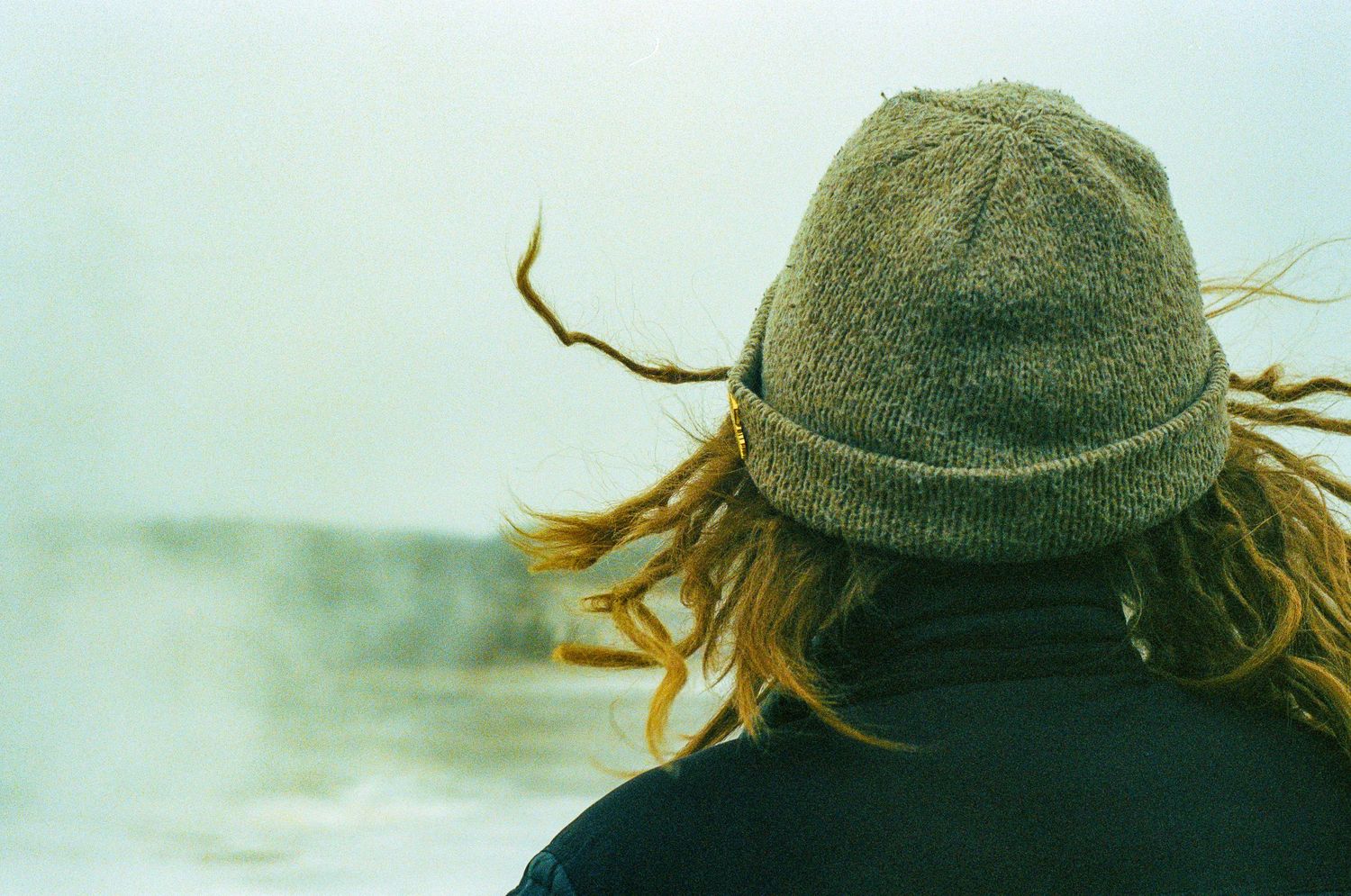 Back view of someone wearing a green beanie hat looking out at a misty view.