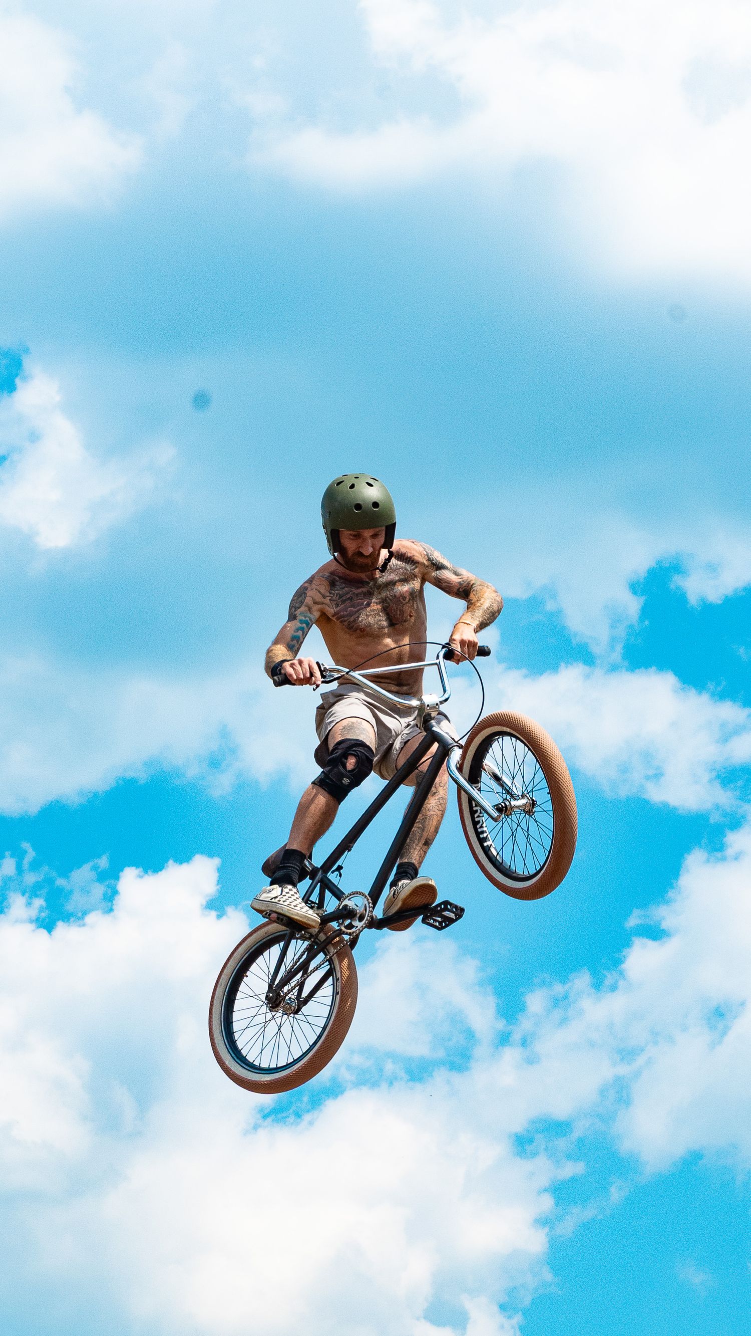 BMX rider soars through air performing jump tricks against bright blue sky.