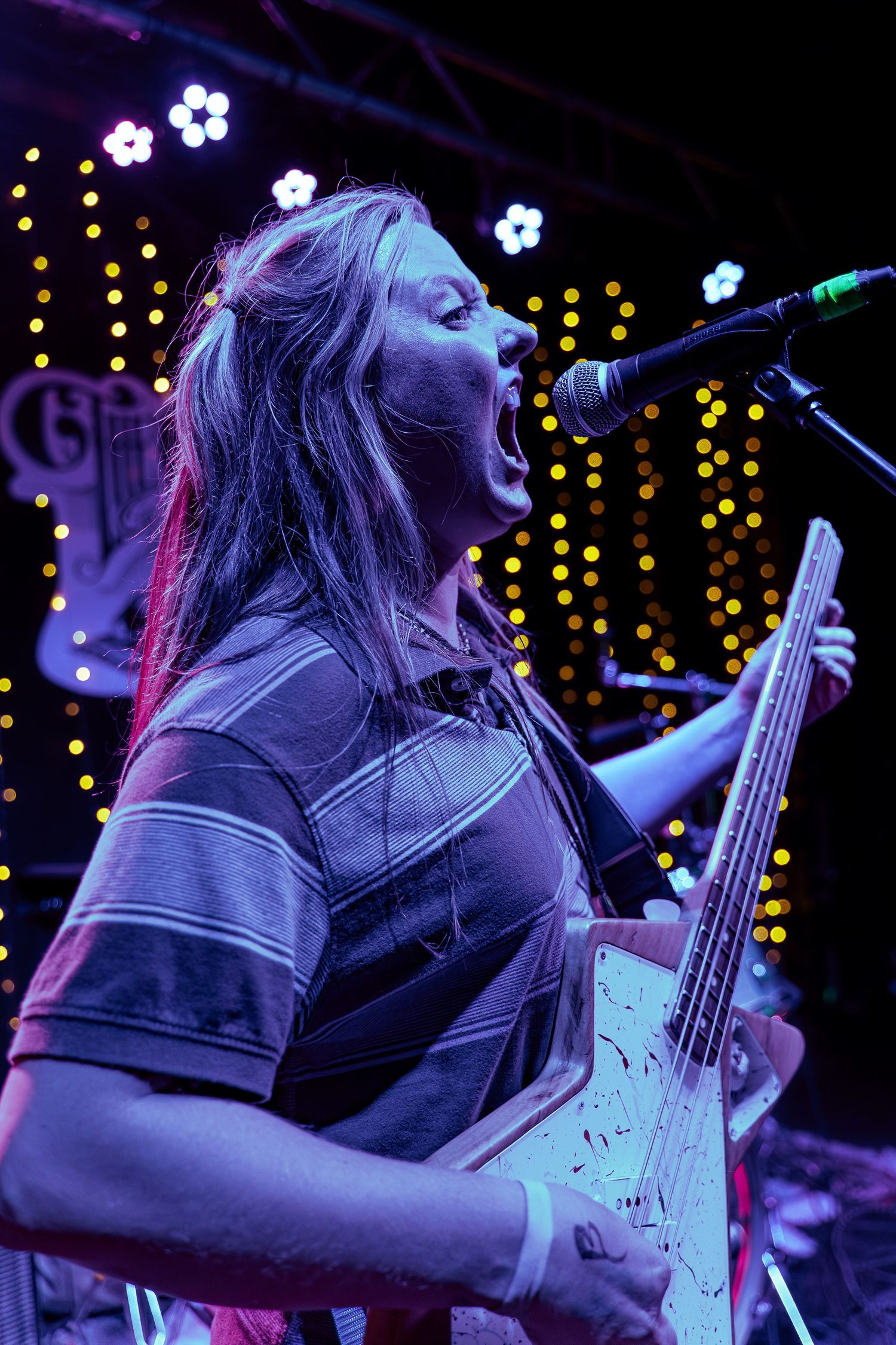 Bass guitar player performs passionately on stage with twinkle lights and purple lighting creating an atmospheric backdrop.