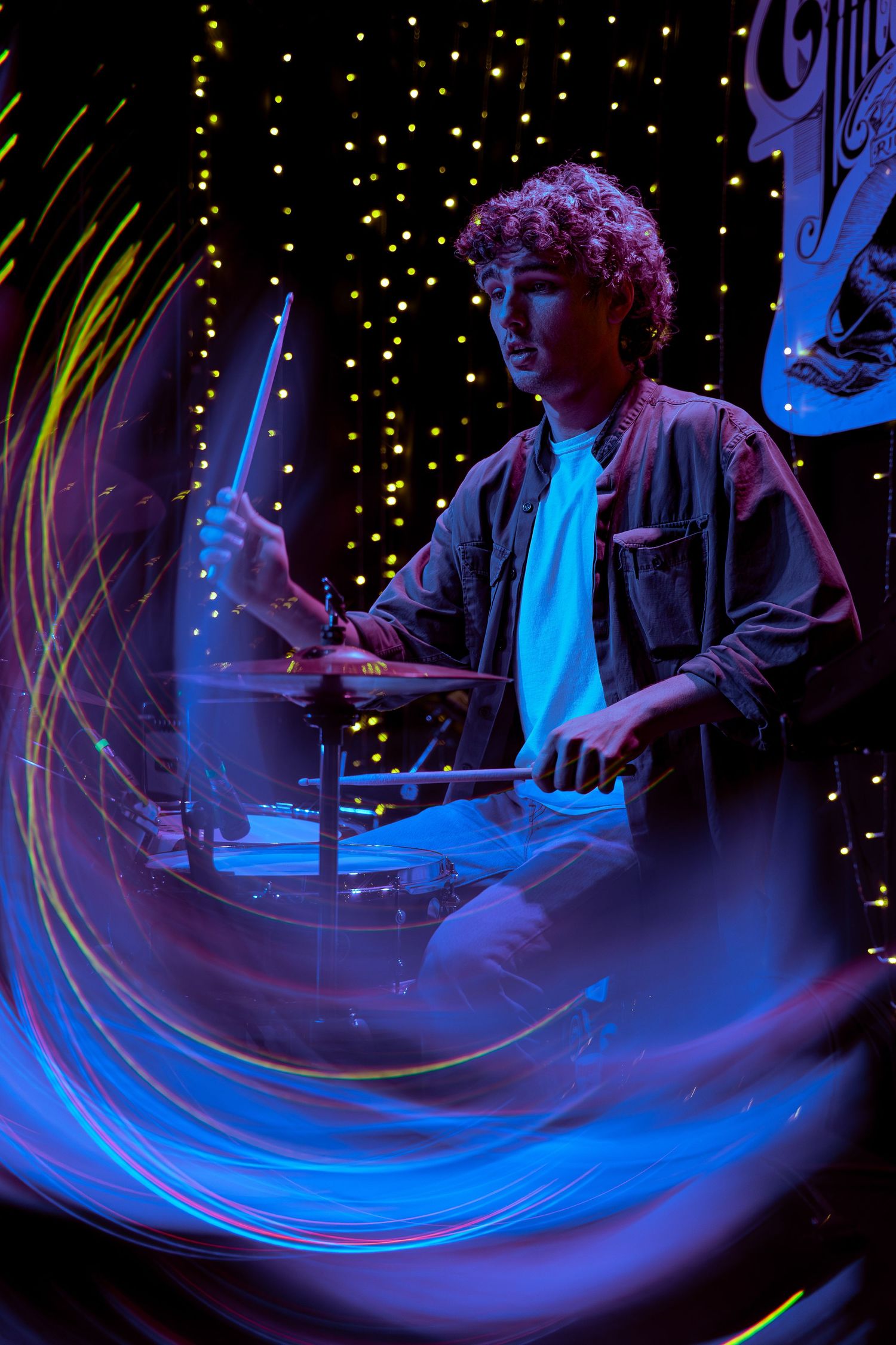 Long exposure shot captures swirling blue light trails during a nighttime drum performance with starry backdrop.
