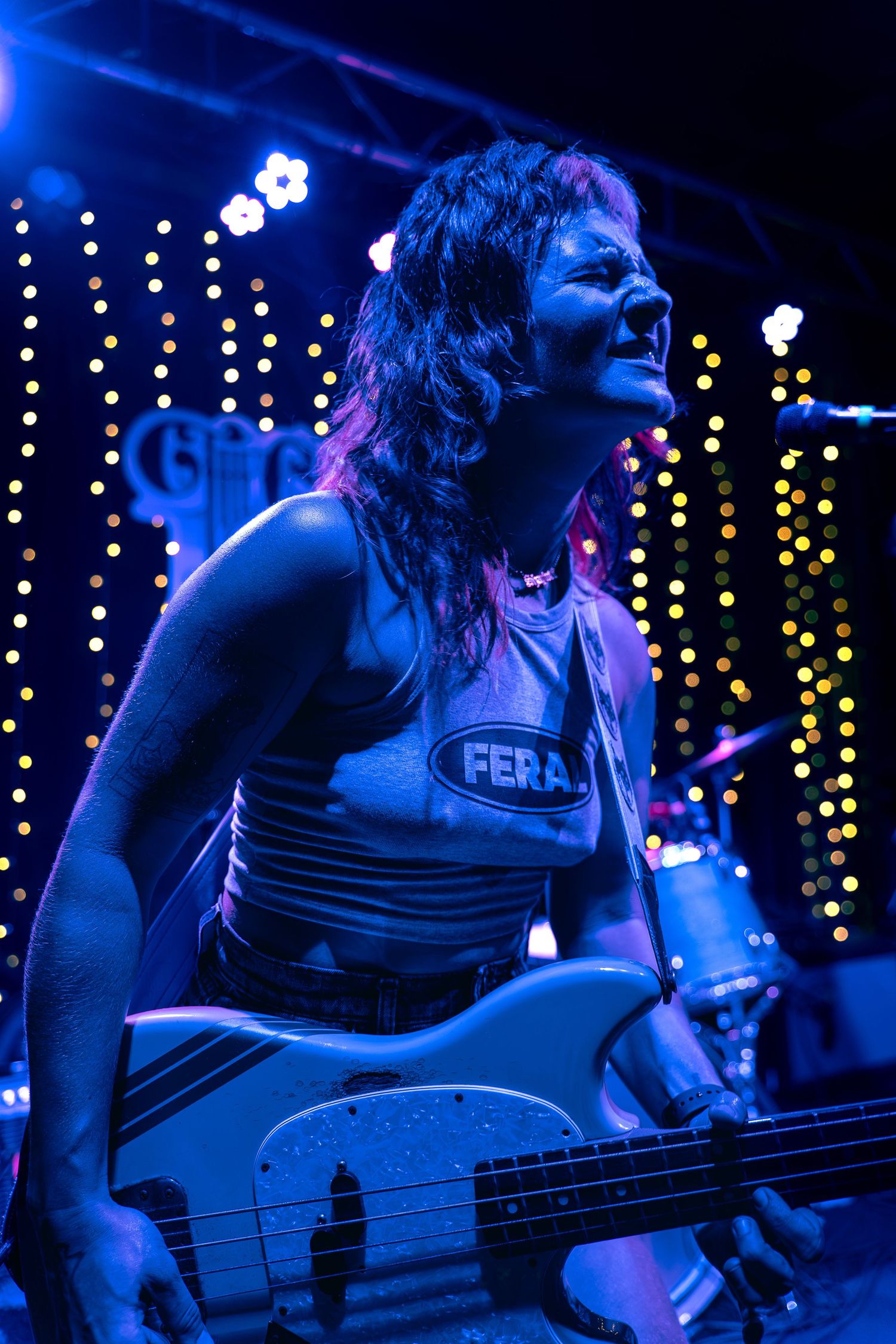Musician plays bass guitar on stage with twinkle lights and blue lighting creating moody atmosphere.