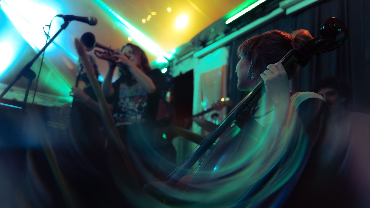 Musicians perform energetically on stage with colorful blue and yellow lighting creating motion blur effects during concert.