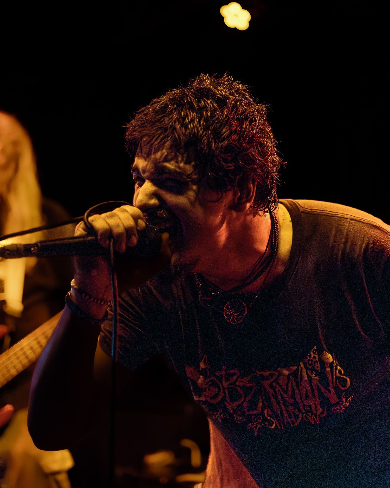 Singer performs with intense emotion on stage in dark atmospheric lighting with orange glow in the background.