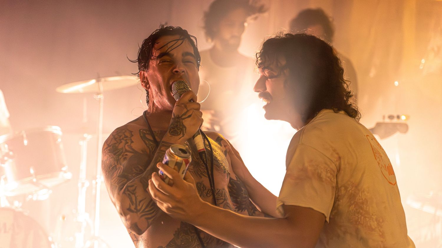 Two performers share an intense moment on stage with dramatic orange backlighting.
