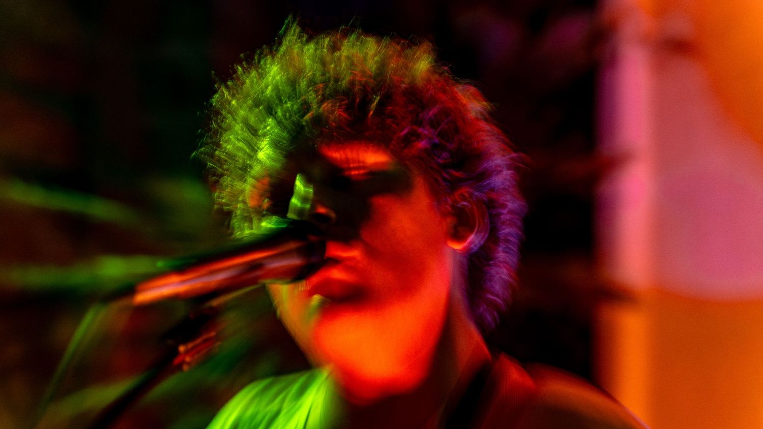 Musician performing on stage illuminated by vibrant red and green lighting effects during an energetic concert.