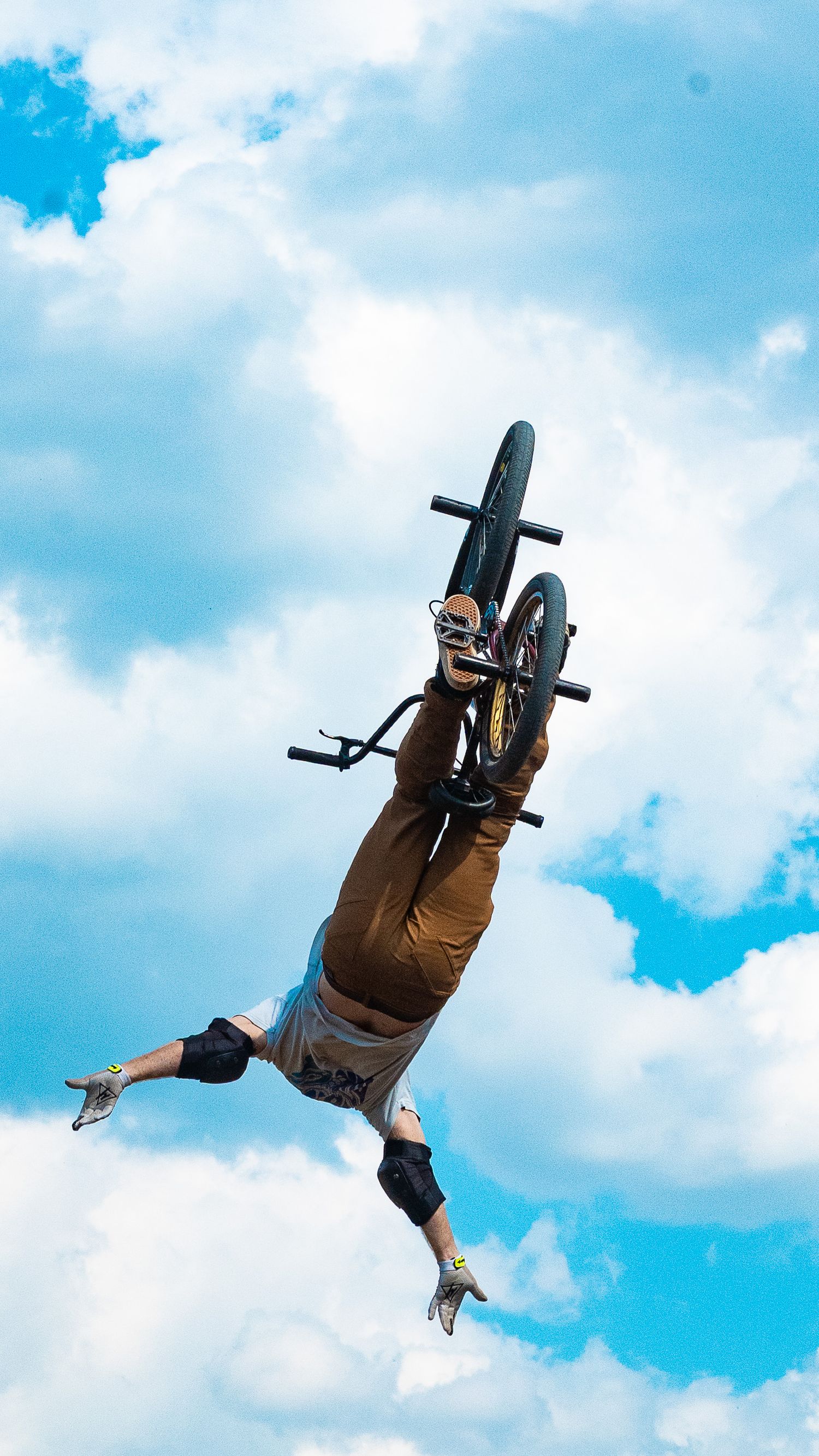 BMX bike and rider silhouetted against bright blue sky during vertical rotation trick.