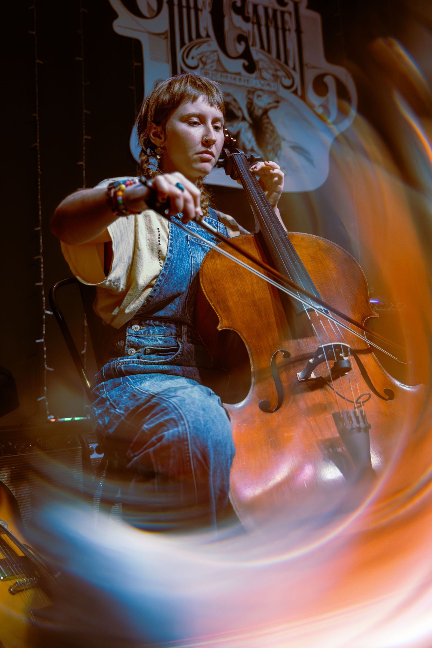 Musician plays cello in dramatic lighting with orange and blue hues creating artistic motion blur effects.