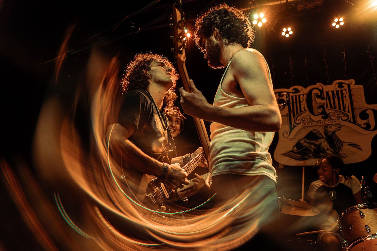 A couple performs an intimate dance move in a dimly lit setting with atmospheric lighting in the background.