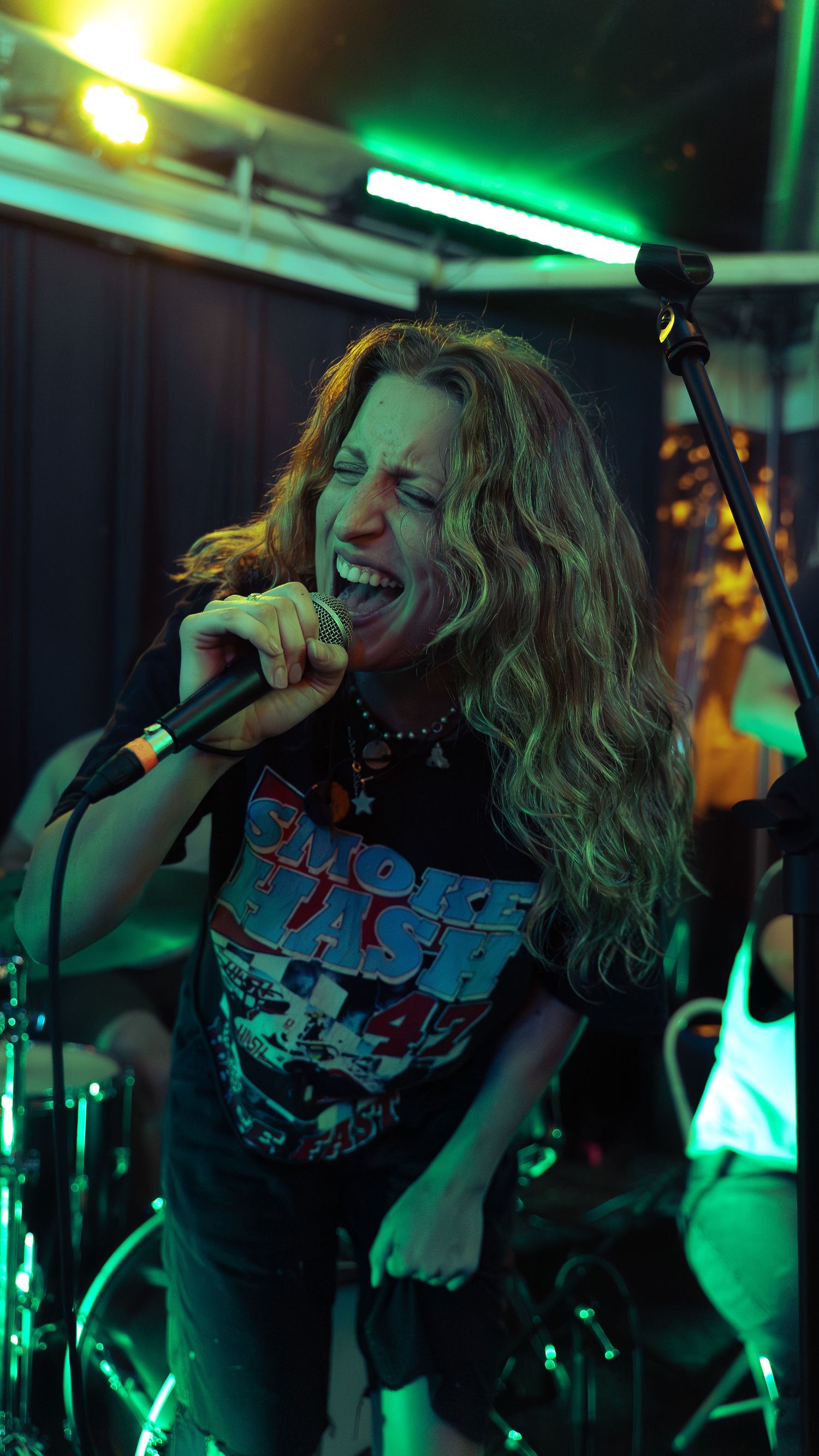 Lead singer performs energetically on stage with band in green-lit venue while wearing a black tank top.