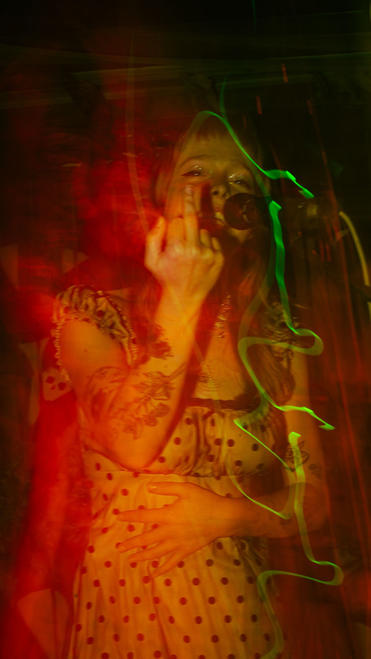 Performer in polka dot dress illuminated by red and green stage lights during energetic show.