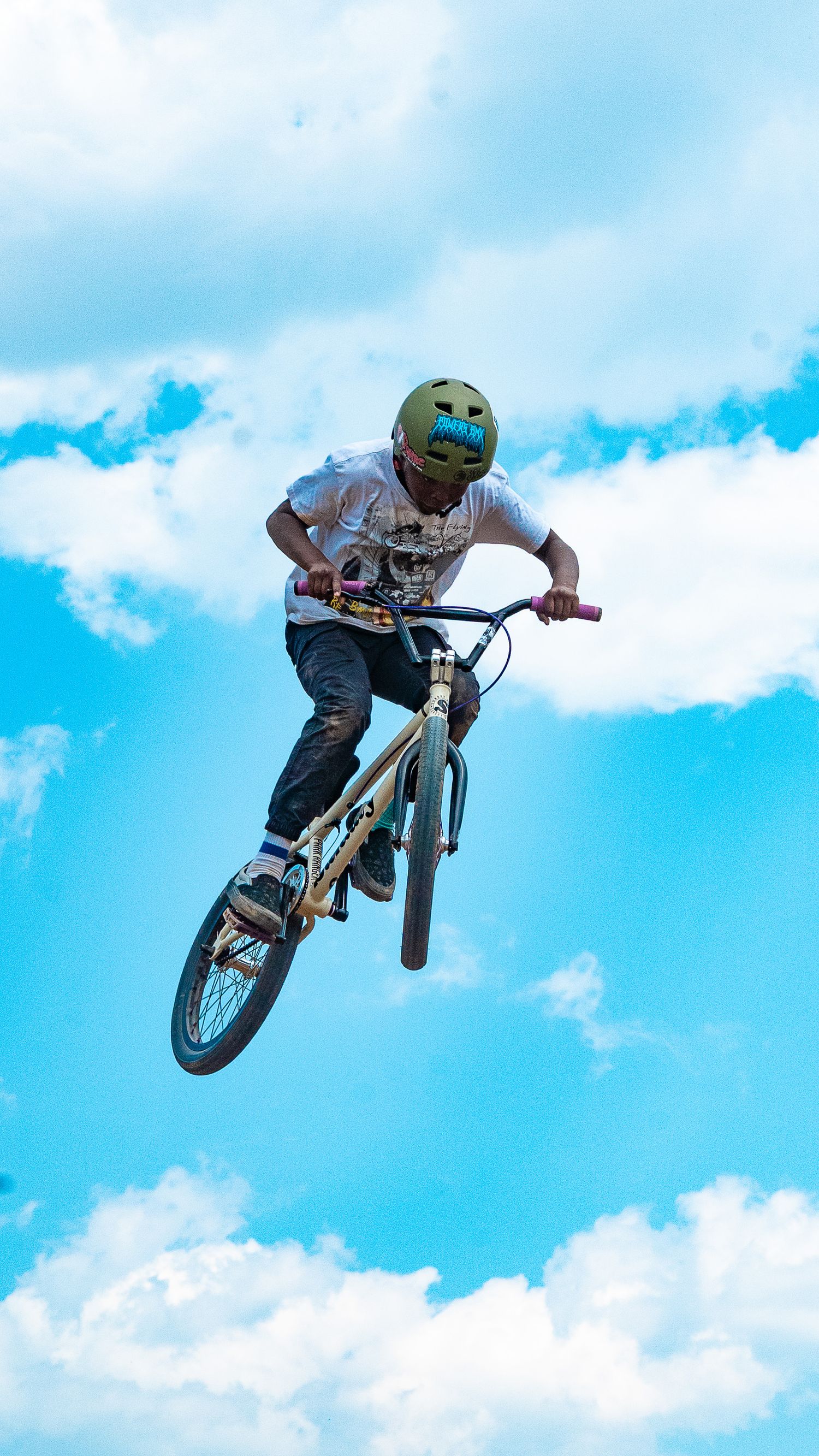 BMX rider performs aerial trick sequence in front of blue sky.