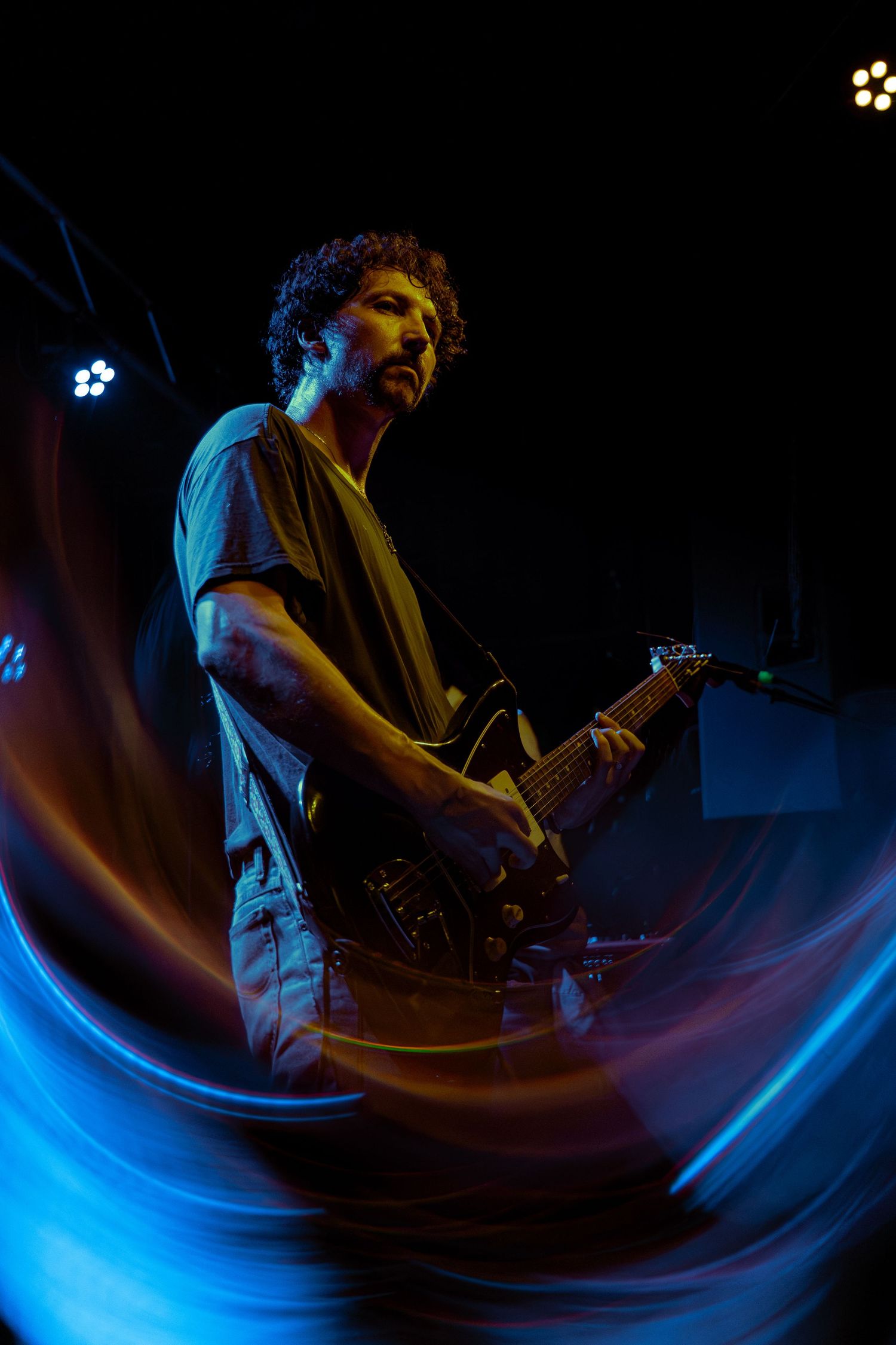 A musician performs on stage with dramatic blue lighting creating motion blur streaks during a live concert performance.