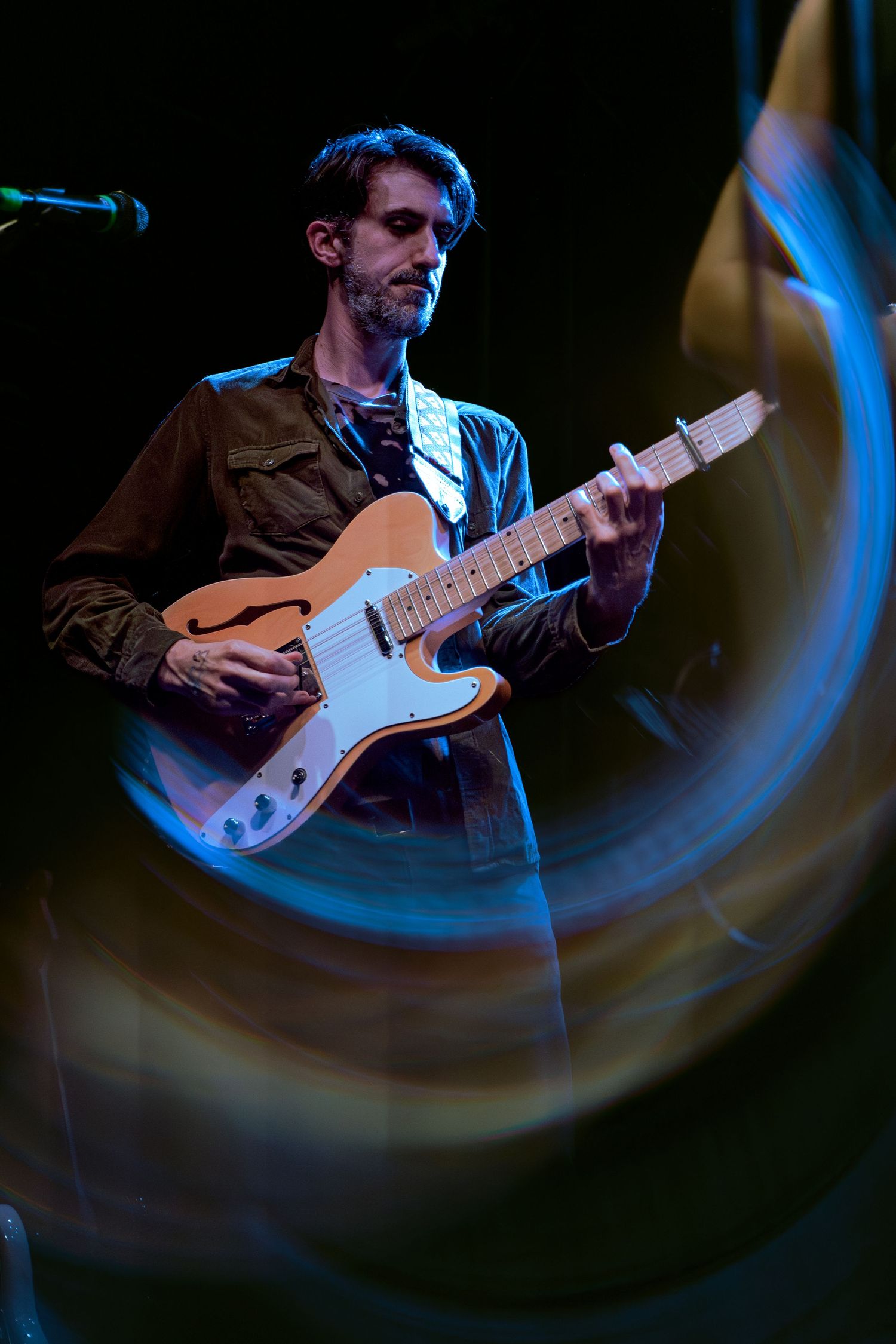 Electric guitar player performing on stage with dramatic blue lighting and motion blur effects in the background.