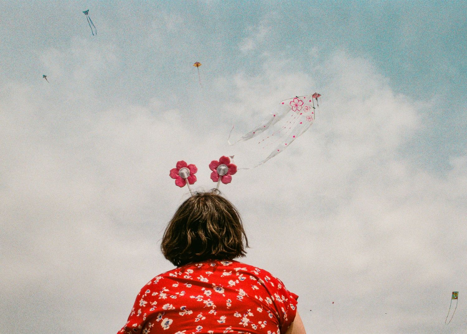 Person wearing red floral dress looks up at cloudy sky with flower decorations floating above.